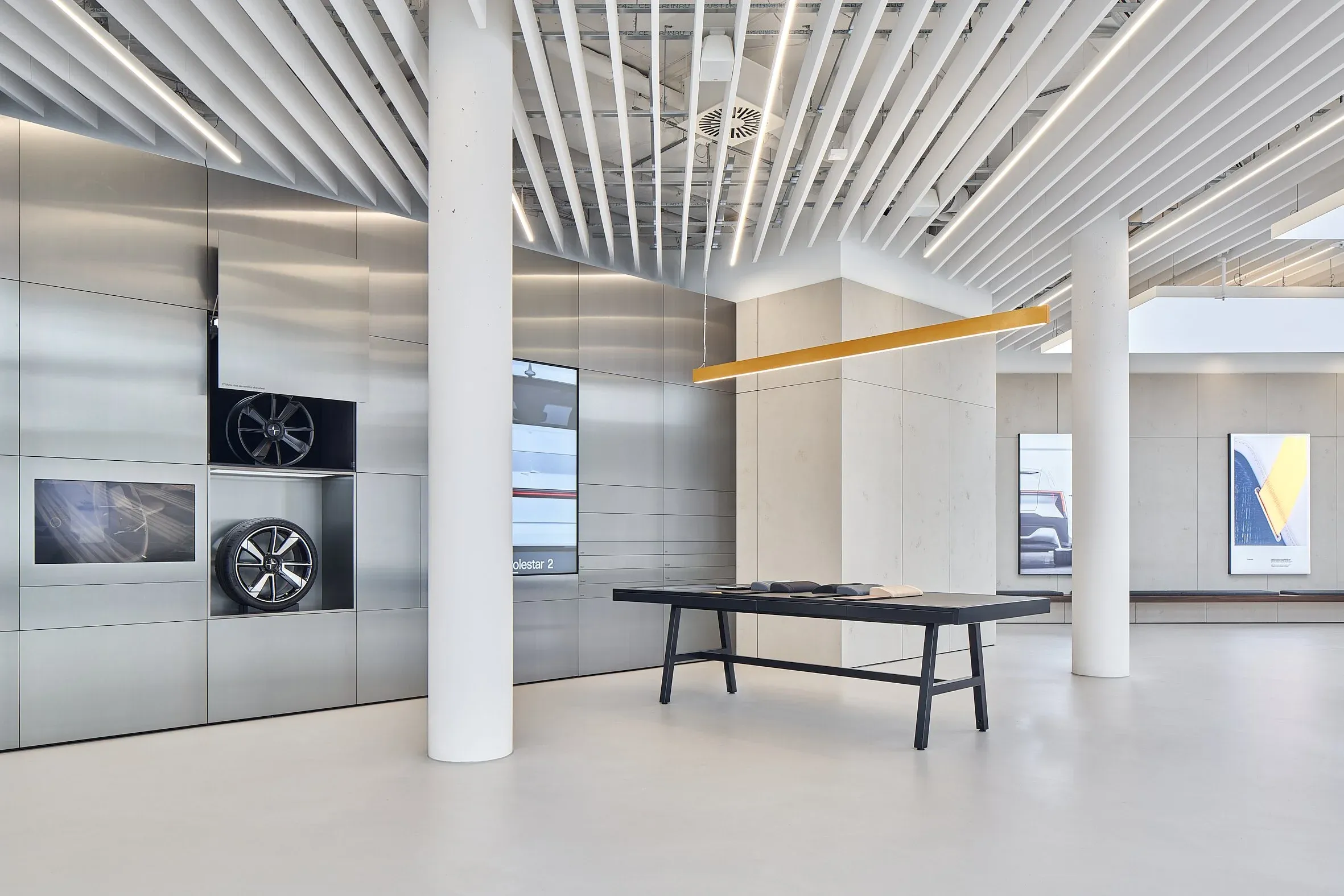 Innenraum des Showrooms, Materialwand mit Felgen links, schwarzer Tisch und beleuchtete Bildtafeln rechts