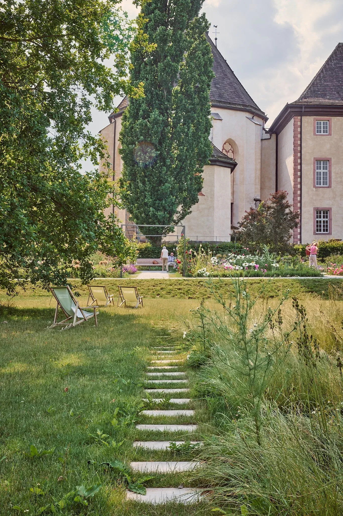 Trittsteinweg durch hohe Wiese im Remtergarten, Liegestühle und blühende Beete vor dem historischen Gebäude