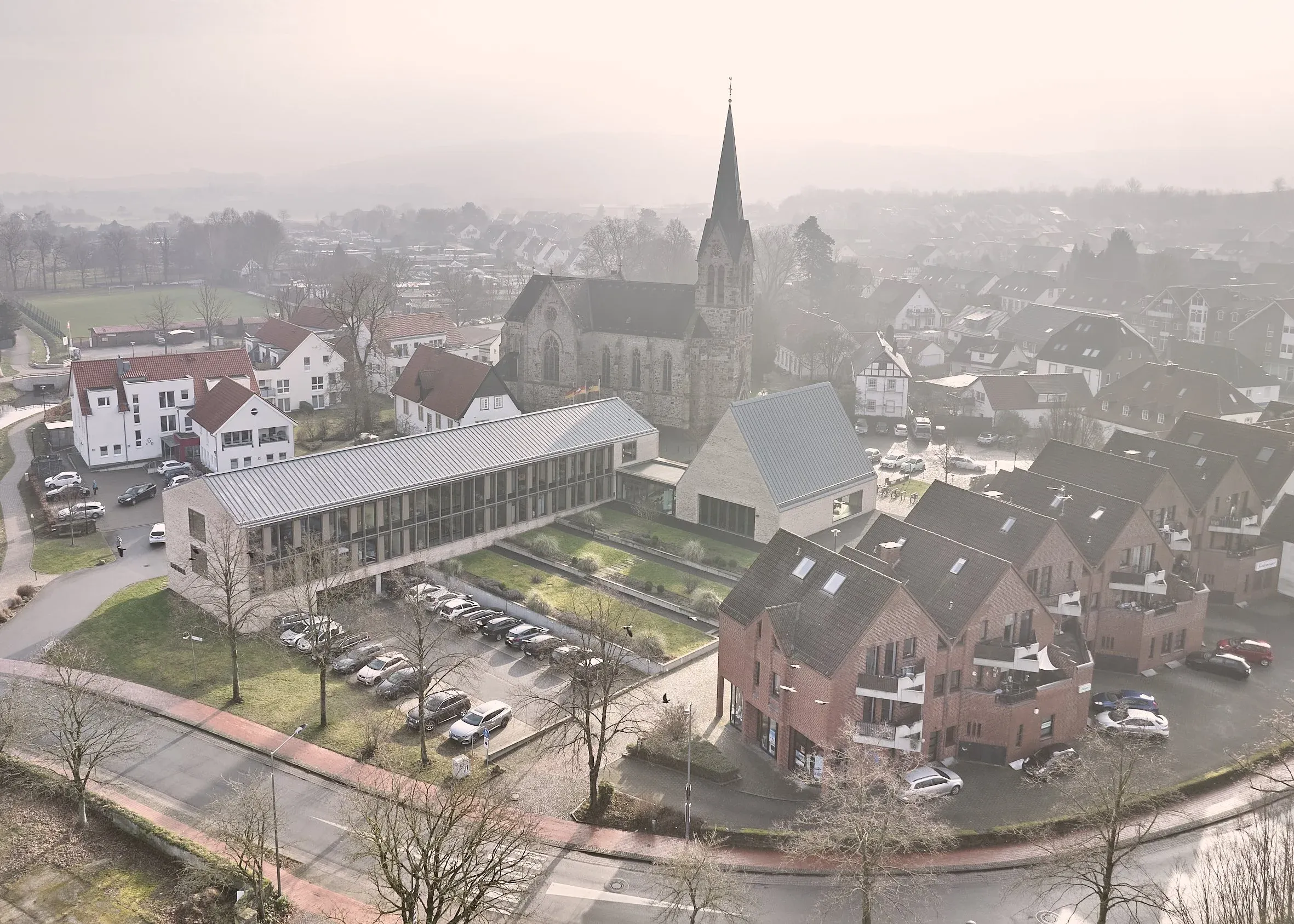 Luftaufnahme von Bissendorf, Blick von oben auf das Rathaus mit Parkplatz, die Kirche und umliegende Wohnbebauung im Dunst