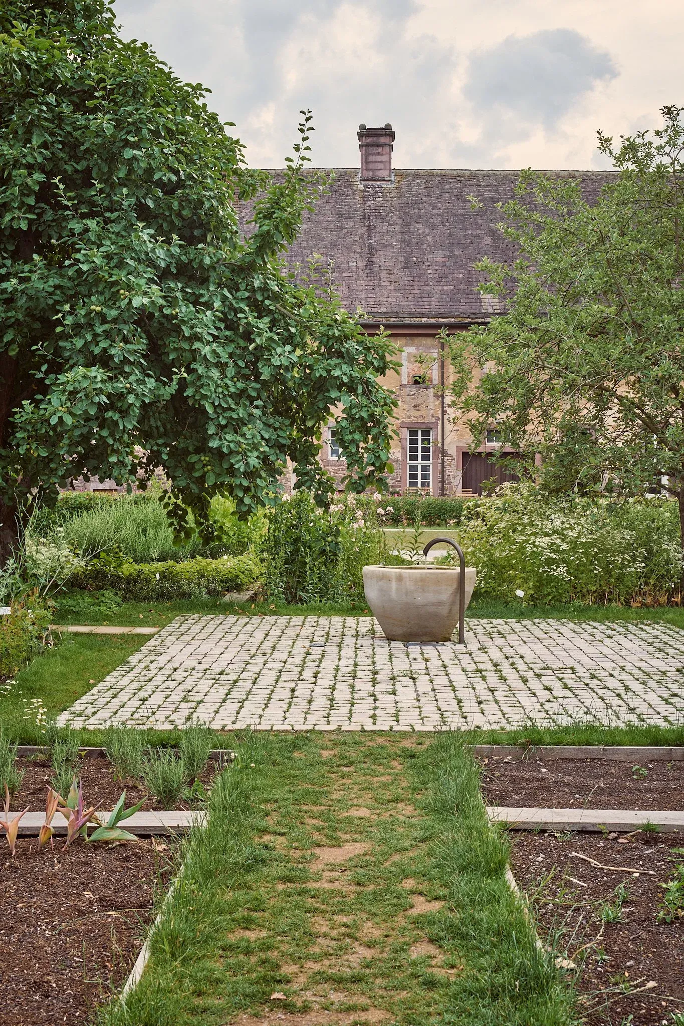Steinbrunnen auf gepflastertem Feld im Remtergarten, Grasweg und Beete vor der alten Fassade