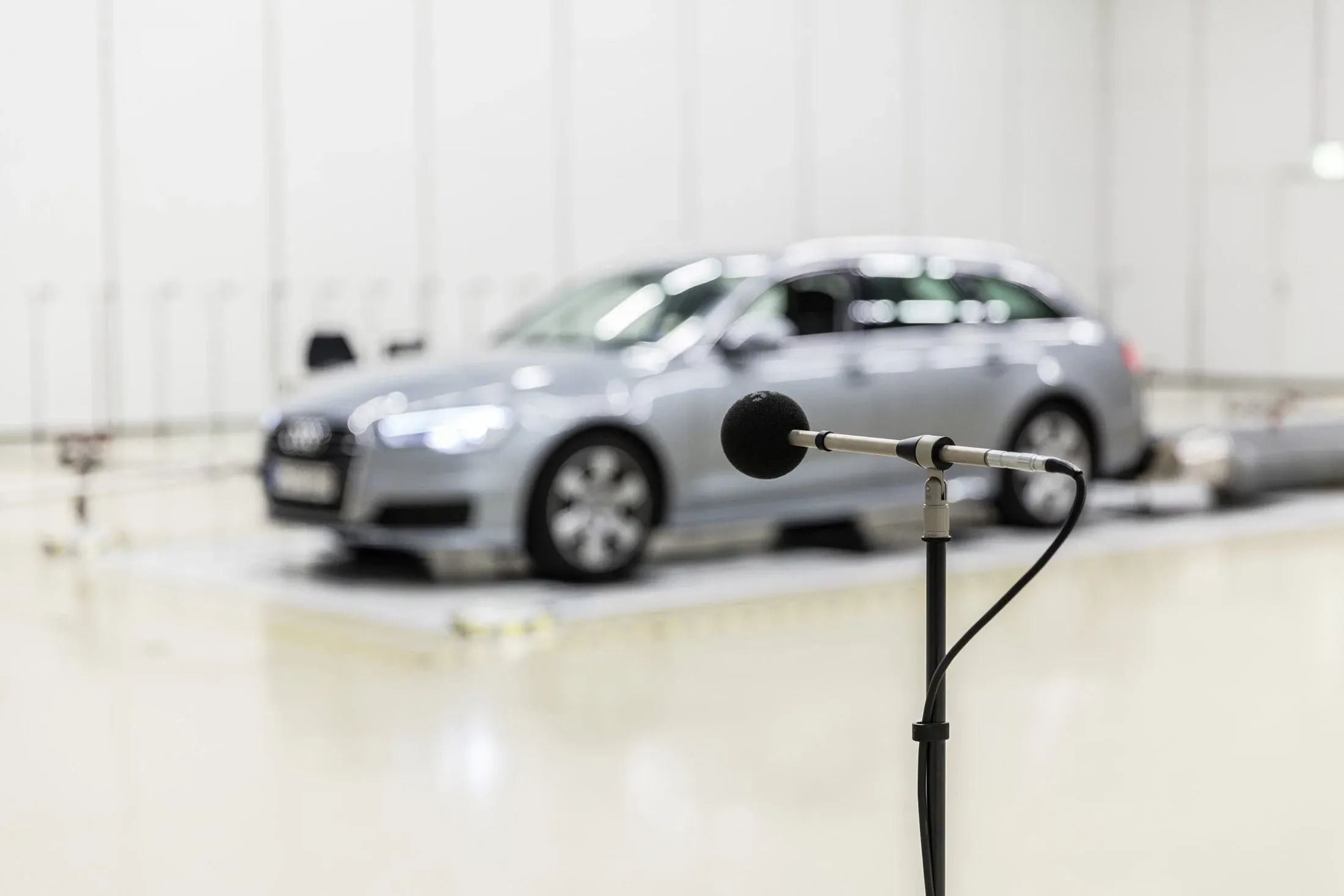 Messmikrofon im Vordergrund scharf, dahinter unscharf ein silbernes Fahrzeug in einer hellen Prüfkammer