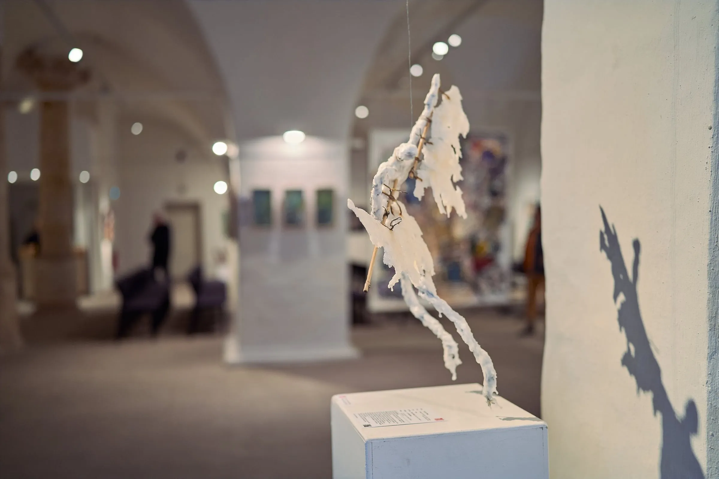 Weiße, filigrane Skulptur auf Sockel, dahinter unscharf der gewölbte Ausstellungssaal mit Werken