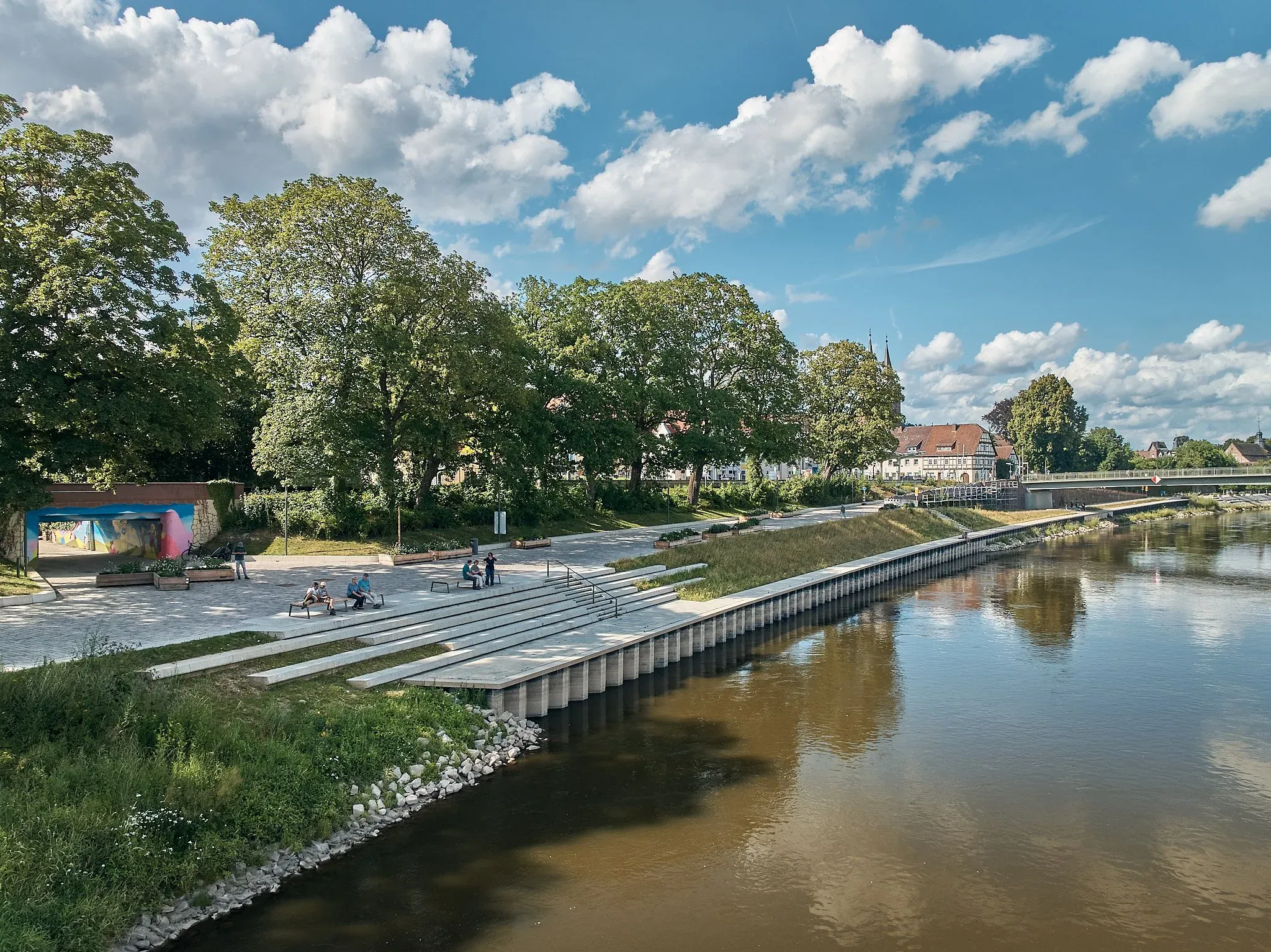 Uferpromenade mit Sitzstufen am Wasser, gespiegelte Bäume und Bebauung in der Weser, Wolkenhimmel