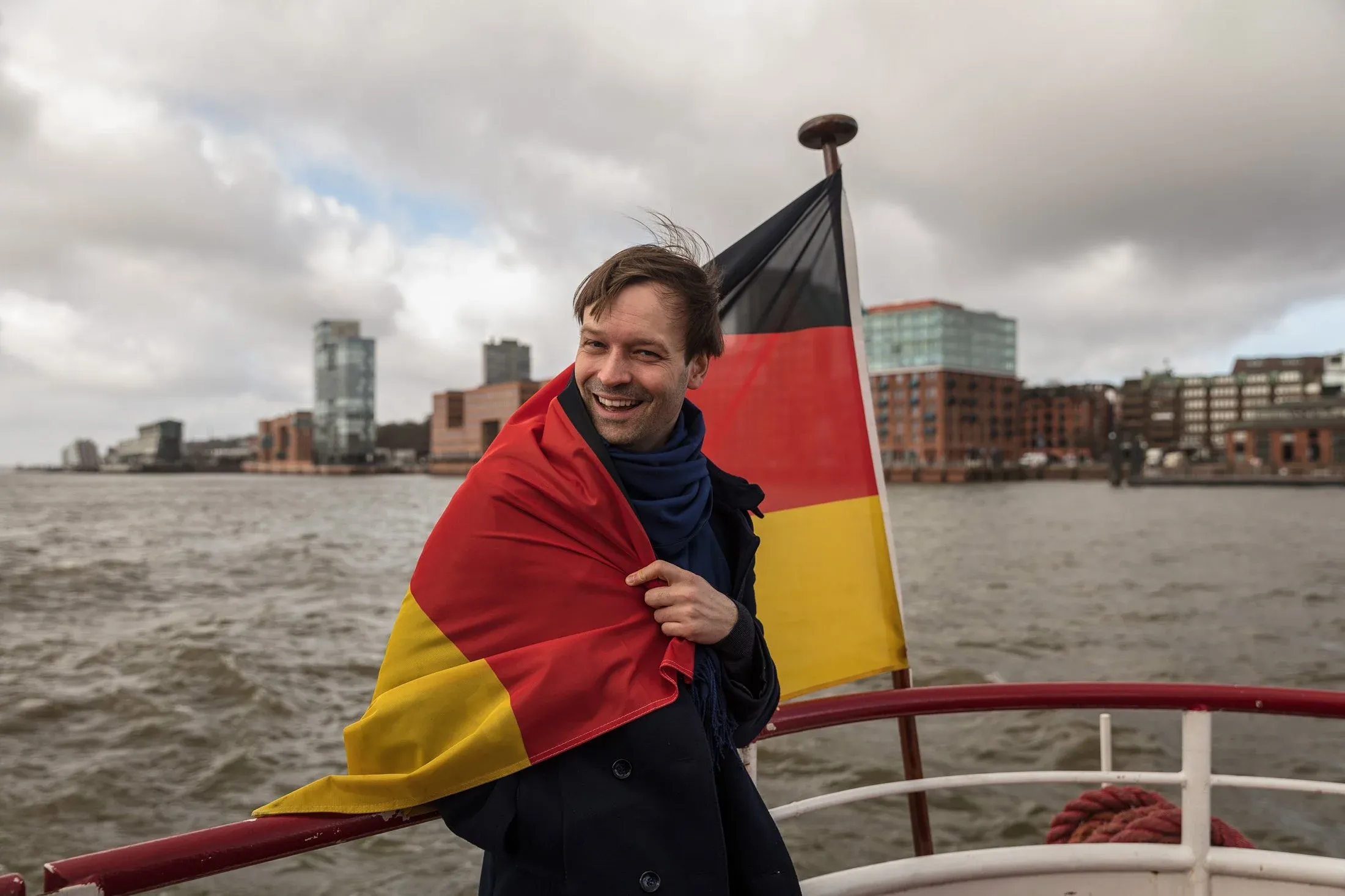 Lachender Mann in eine Fahne gehüllt an Bord eines Schiffes auf der Elbe