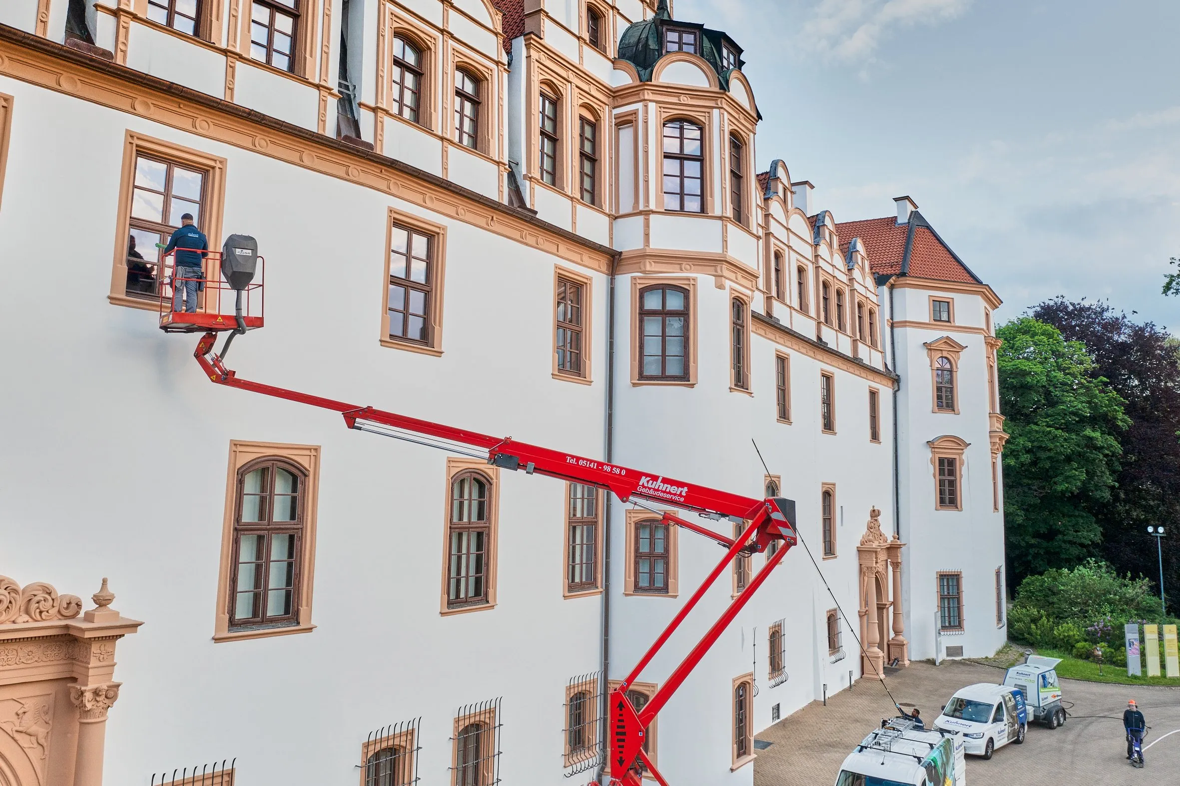 Mitarbeiter reinigt von einer roten Hebebühne die Fenster der Celler Schlossfassade, Fahrzeuge davor