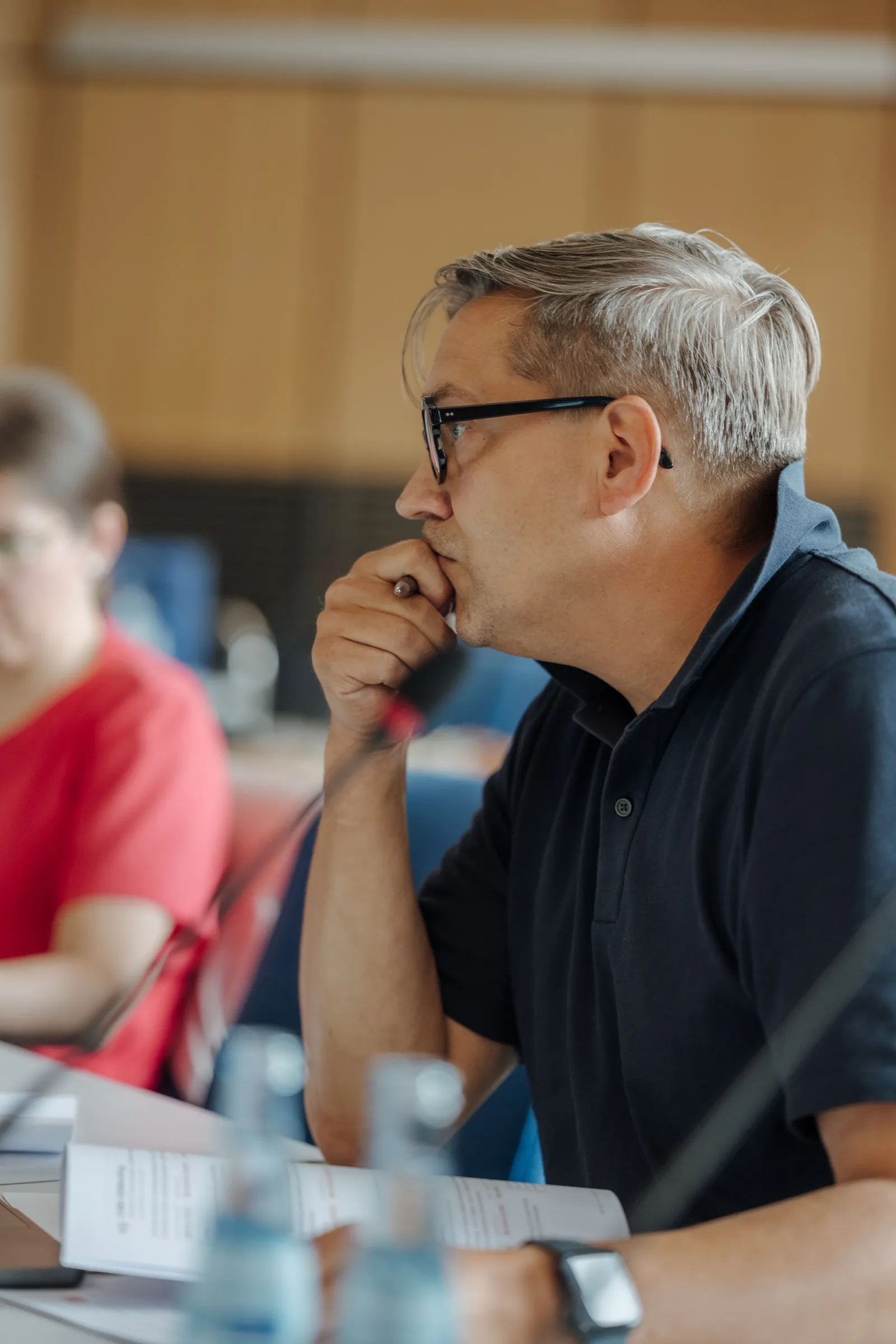 Roman Thomas in profile at the session table, hand on his chin, listening, a microphone and water bottles in the foreground