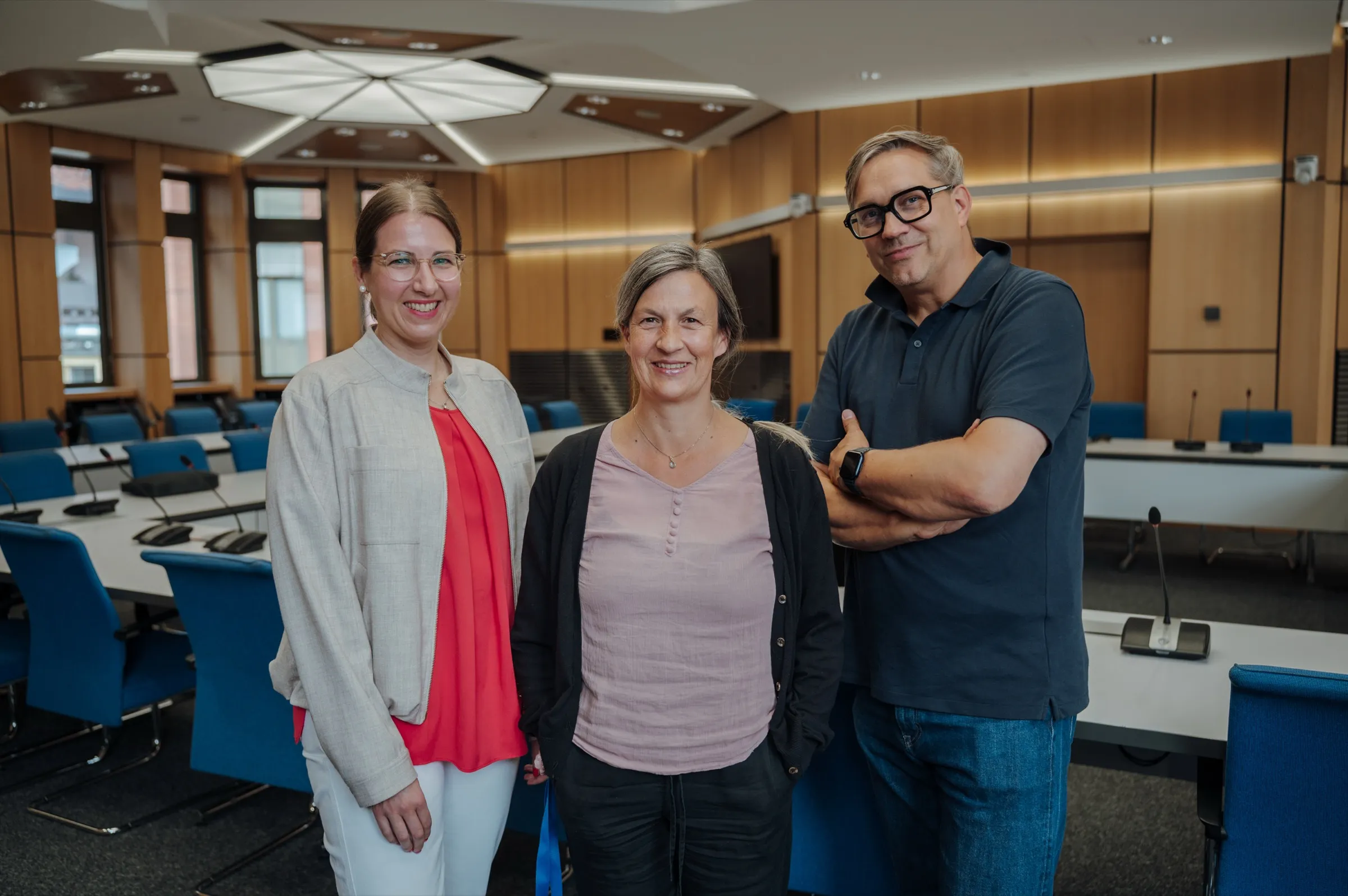 Dr. Anna Heinze, Anne Prenzler and Roman Thomas standing side by side in the session room of the state parliament in front of the rows of tables