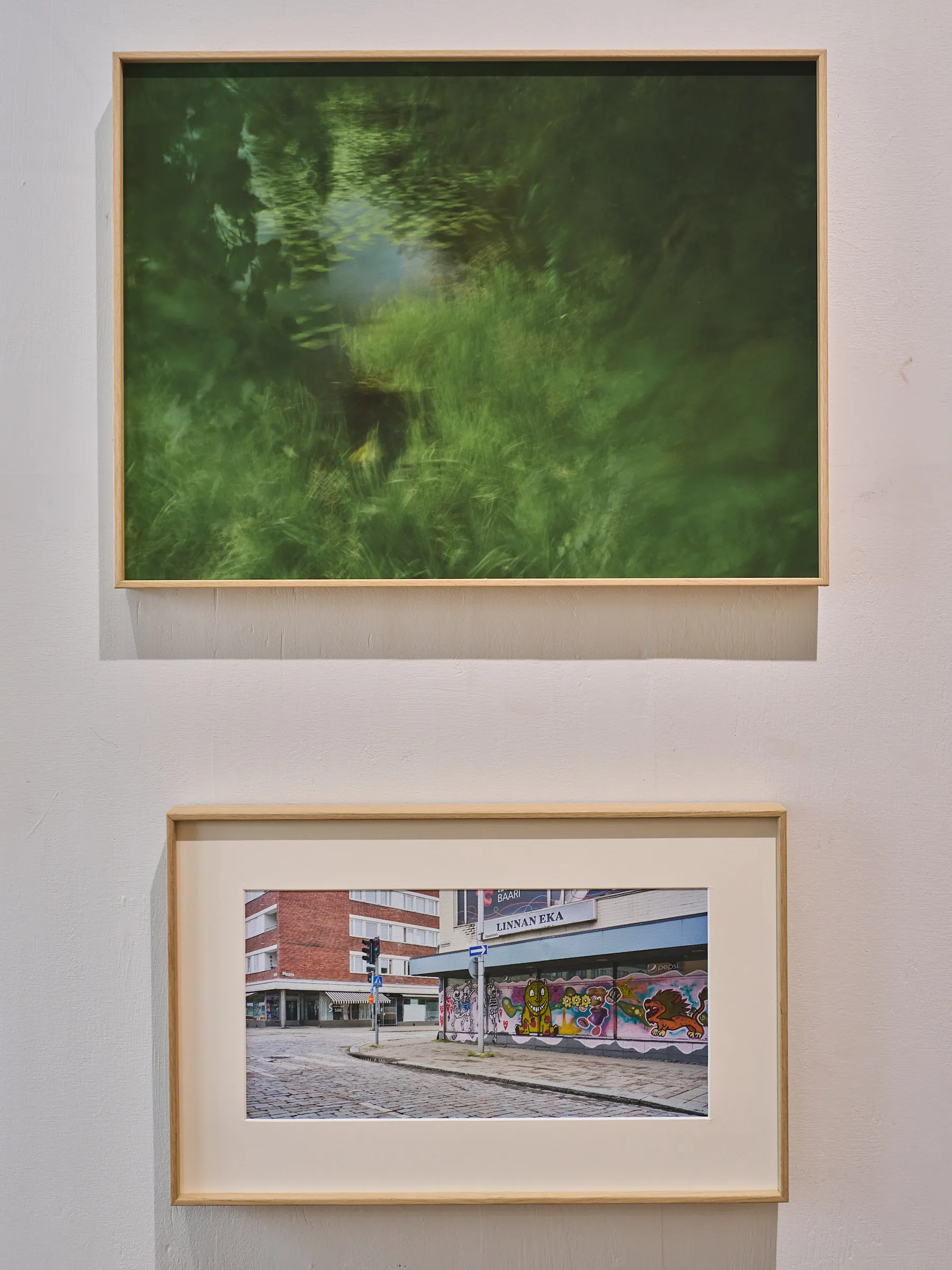 Two framed photographs above one another, a green water picture on top, a street corner with graffiti below
