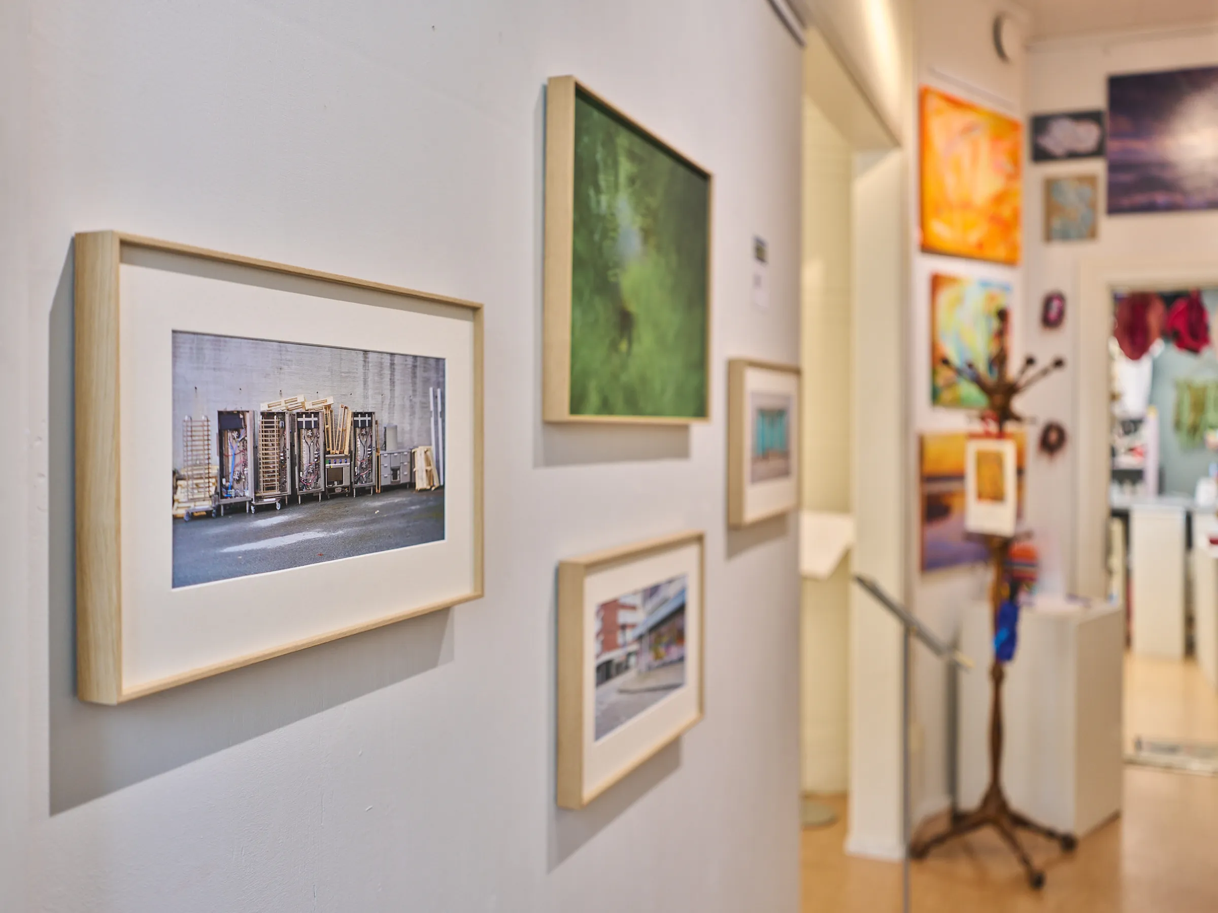 Framed photographs on a wall, a passage behind them into a room with colourful paintings