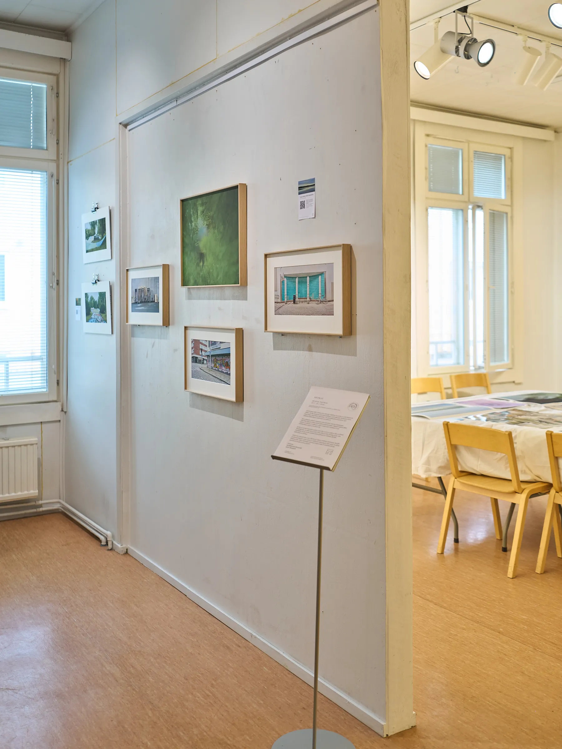 View through a doorway onto the picture wall, a text stand in front, the room with yellow chairs beyond