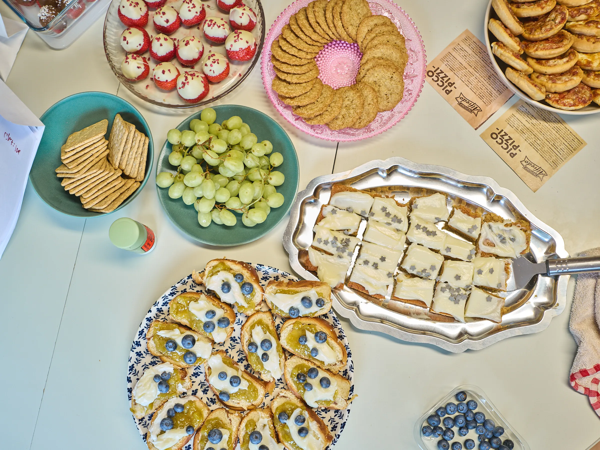 Overhead view of platters with cookies, grapes, crackers and small open sandwiches