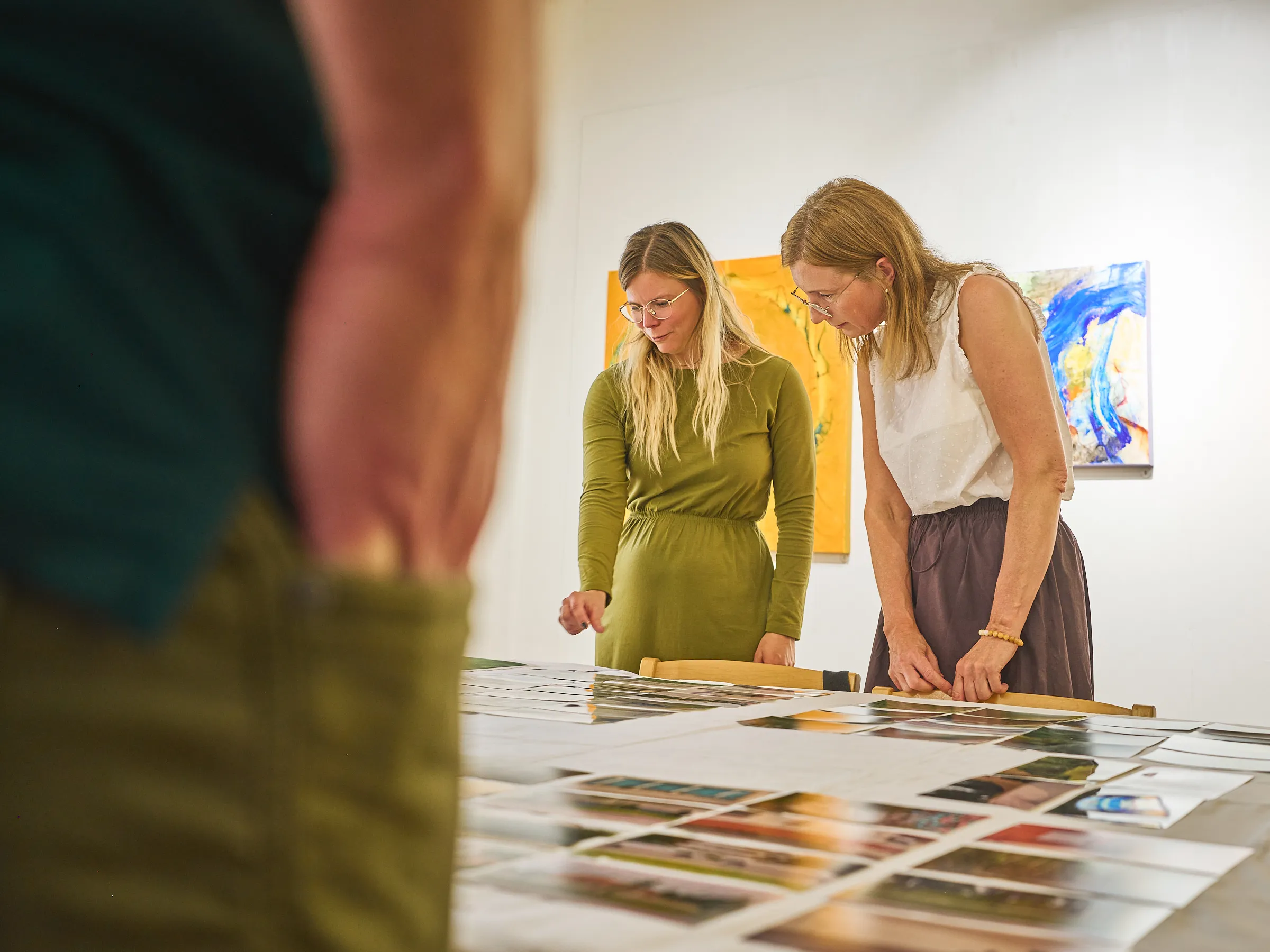 Two women leaning over the photographs laid out and looking at them
