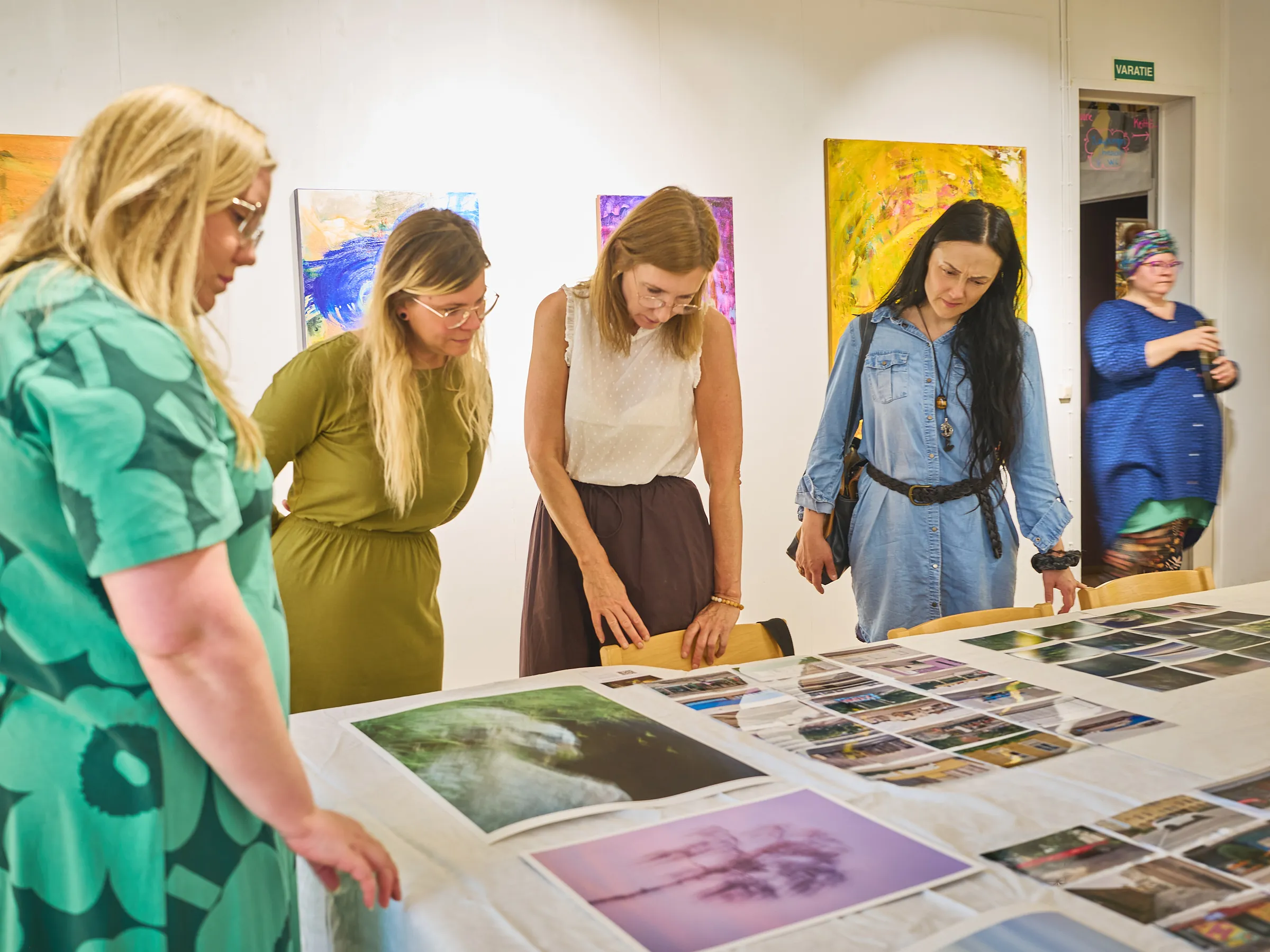 Group of women at the table with the pictures, a green patterned dress in front