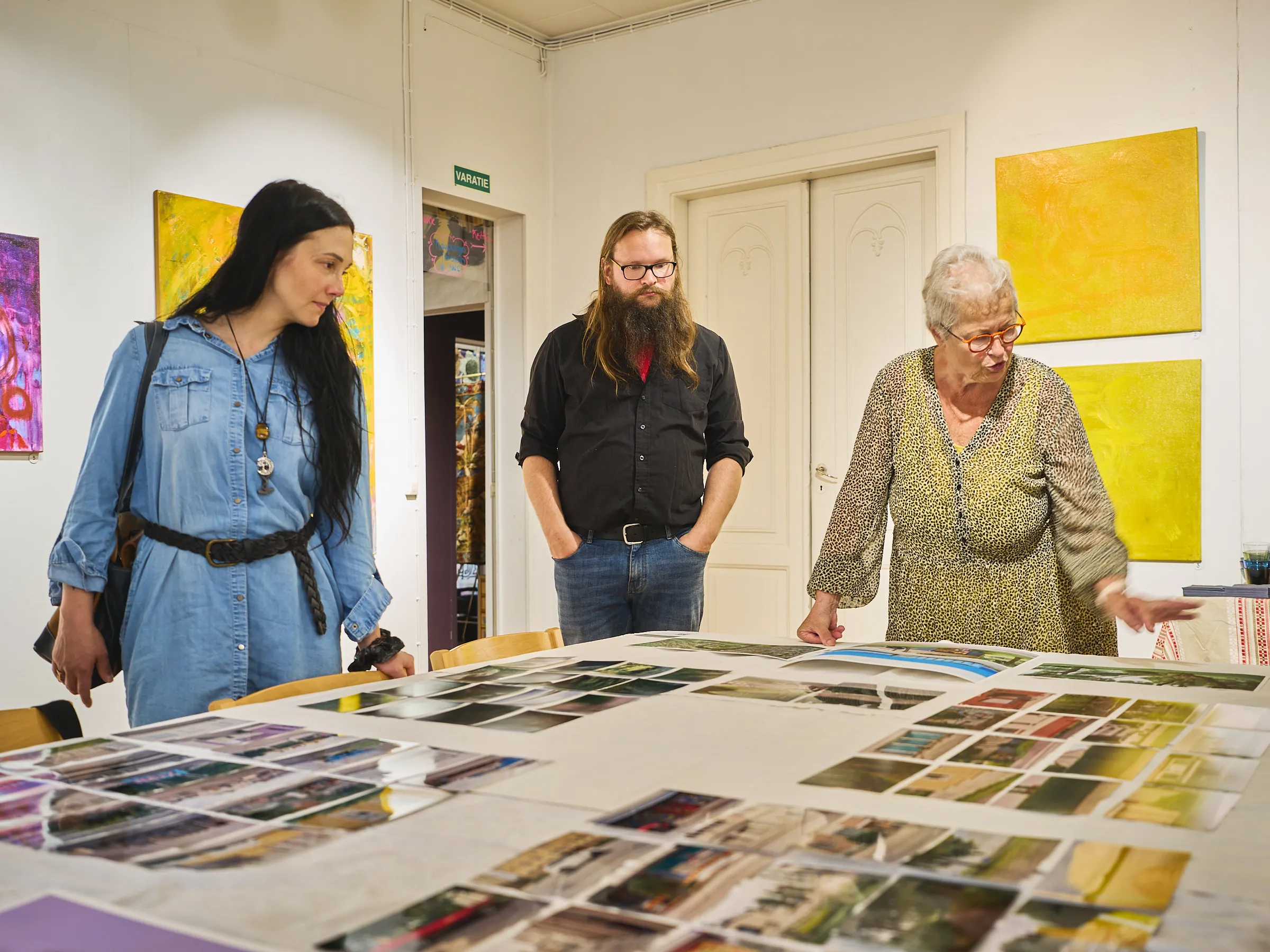Three people standing at the table with the pictures, talking