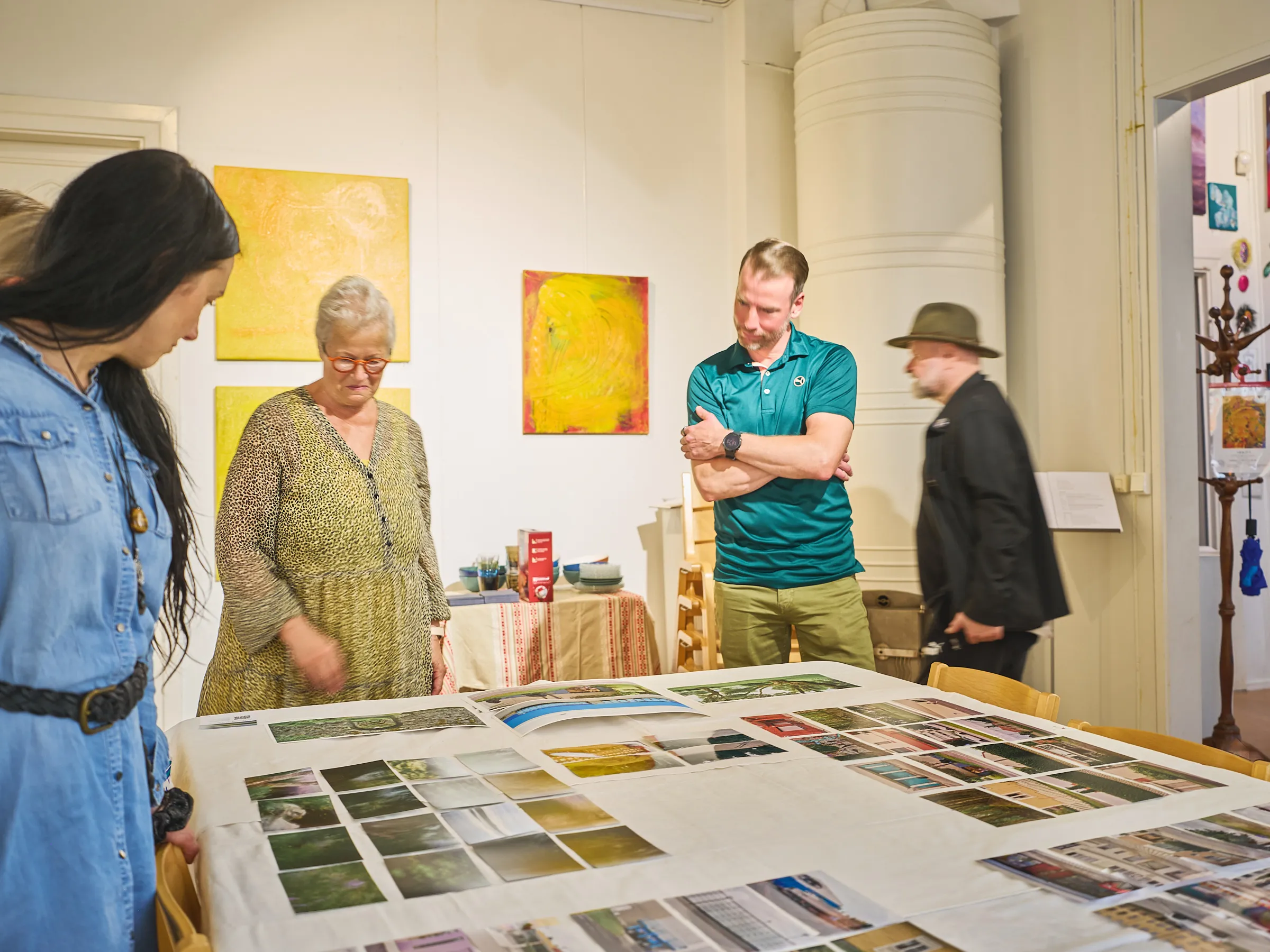 Four people around the table with photographs laid out, yellow paintings in the background