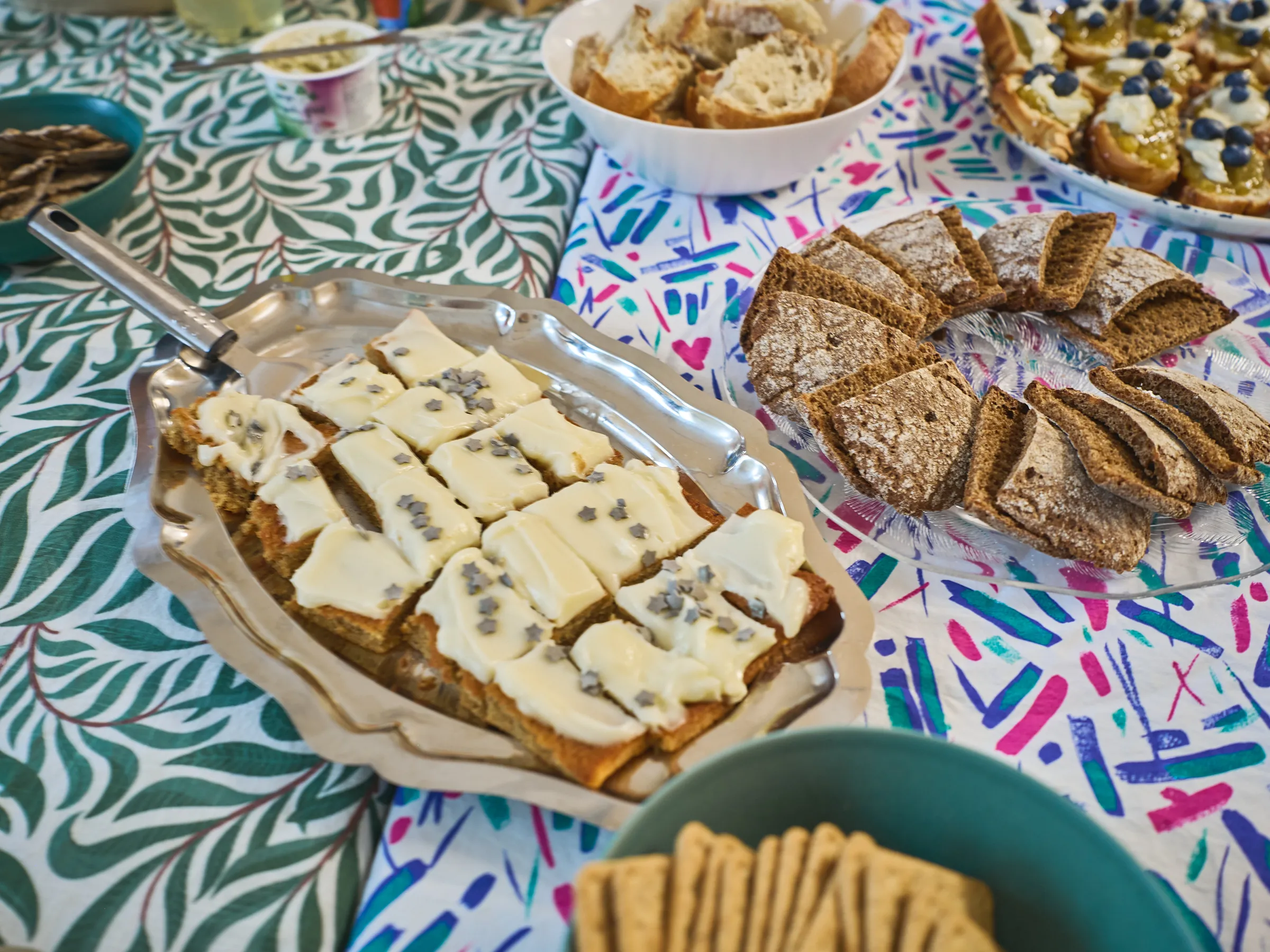 Platters with light and dark bread, topped pieces and a basket of crispbread on a patterned cloth