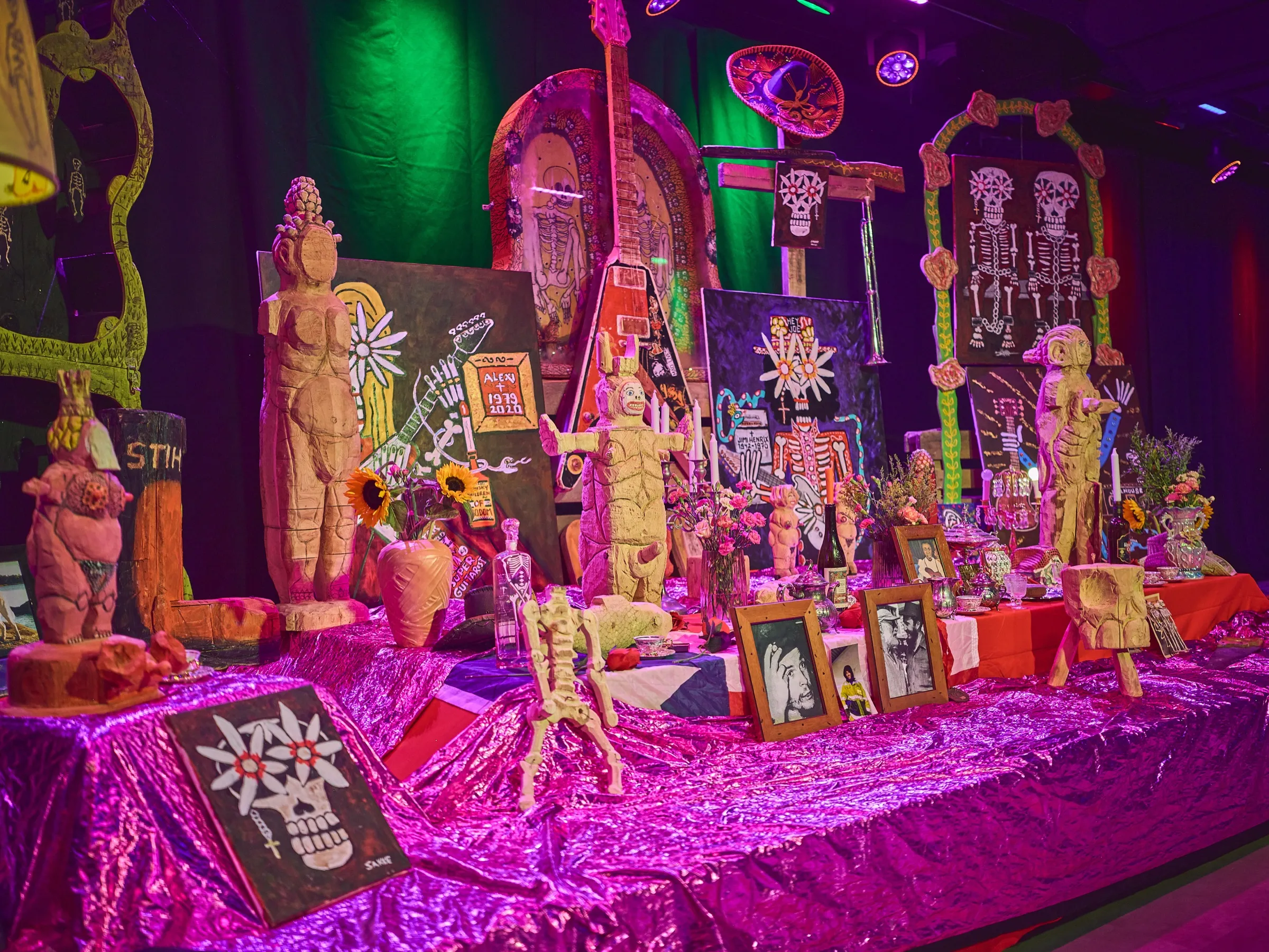 Richly decorated memory altar with figures, candles and framed photos on a shiny pink cloth