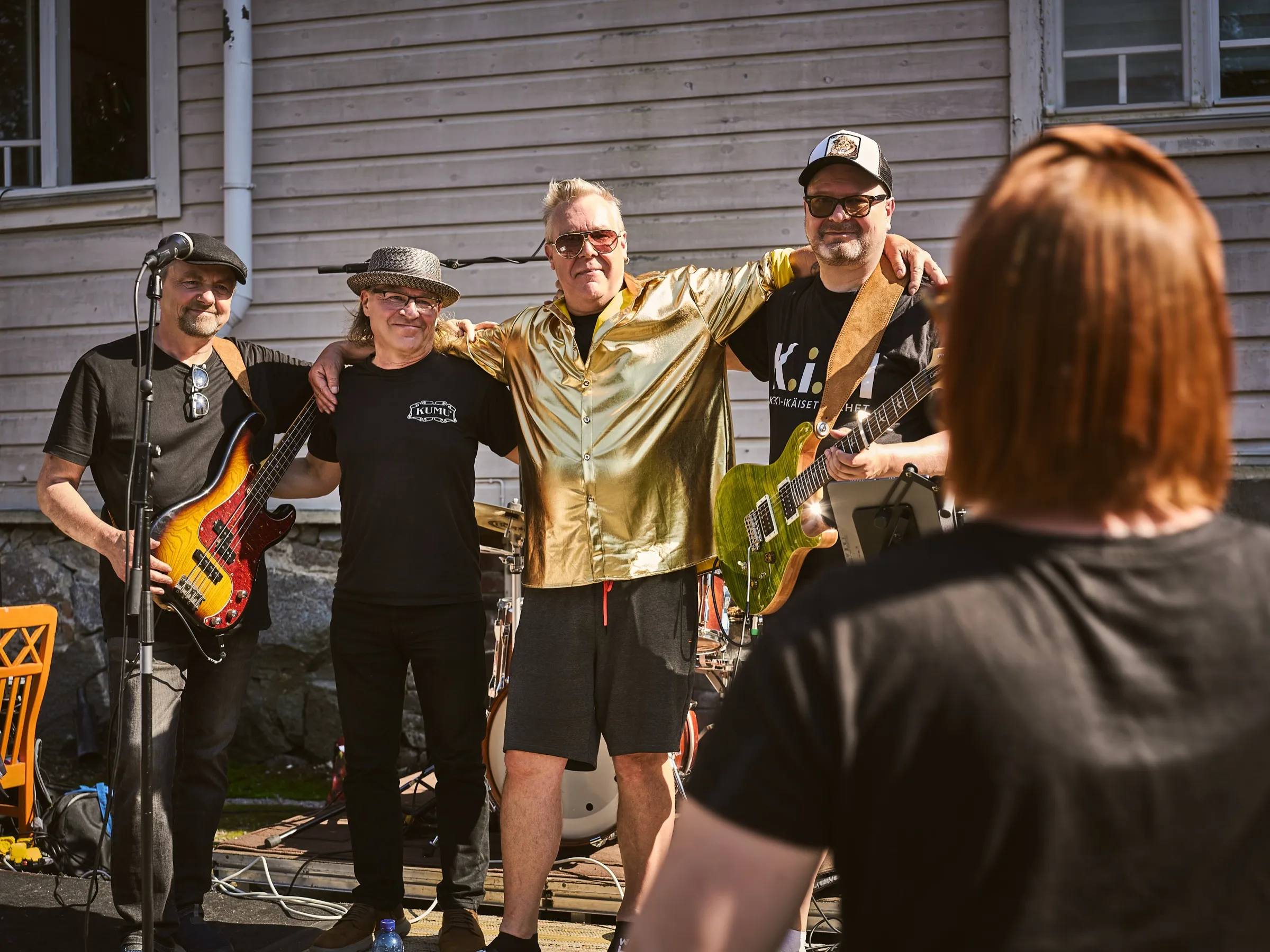 Four musicians of the band standing arm in arm in front of the wooden house, posing for a photo