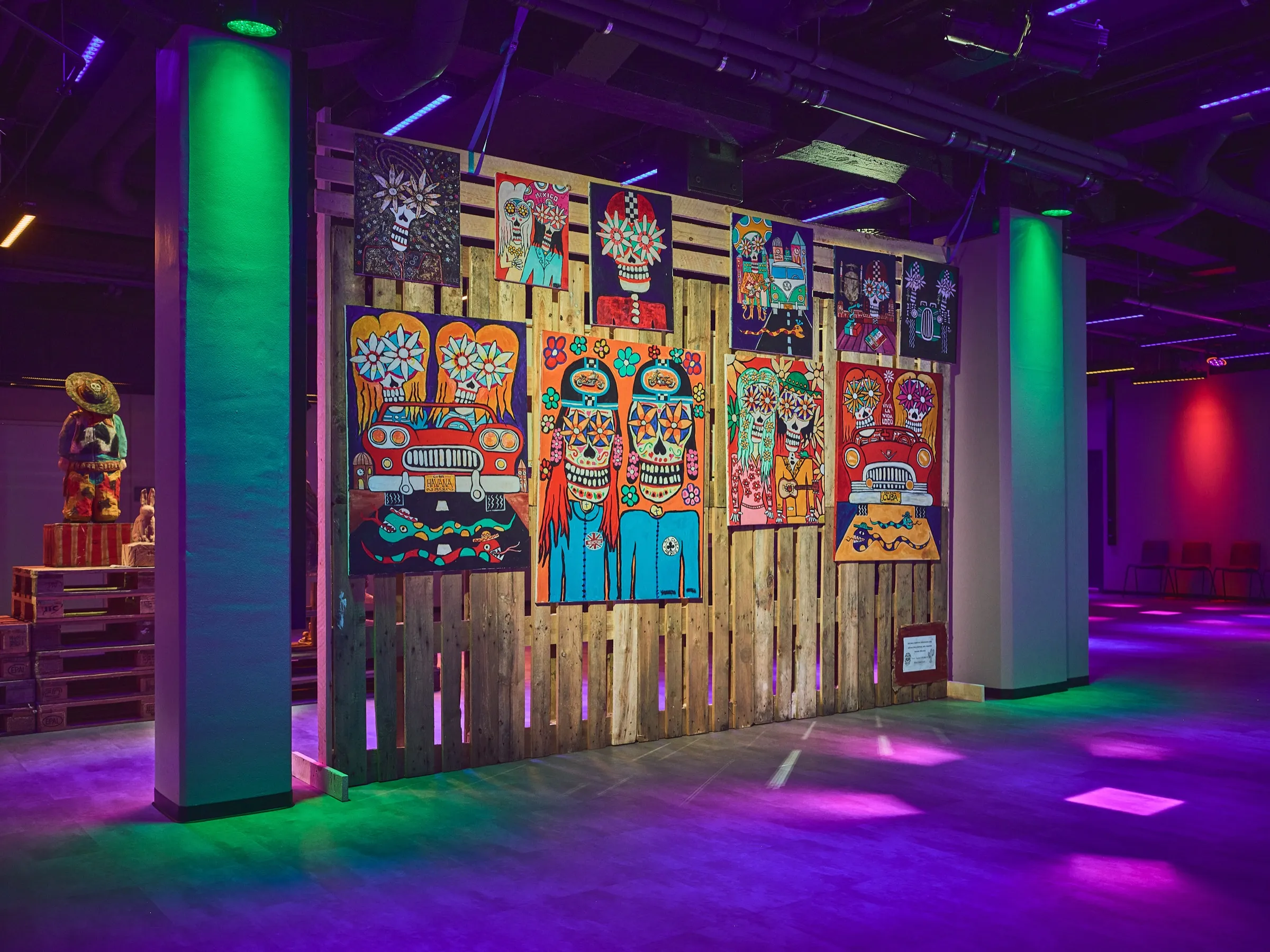 Paintings on pallet wood beside a green-lit column