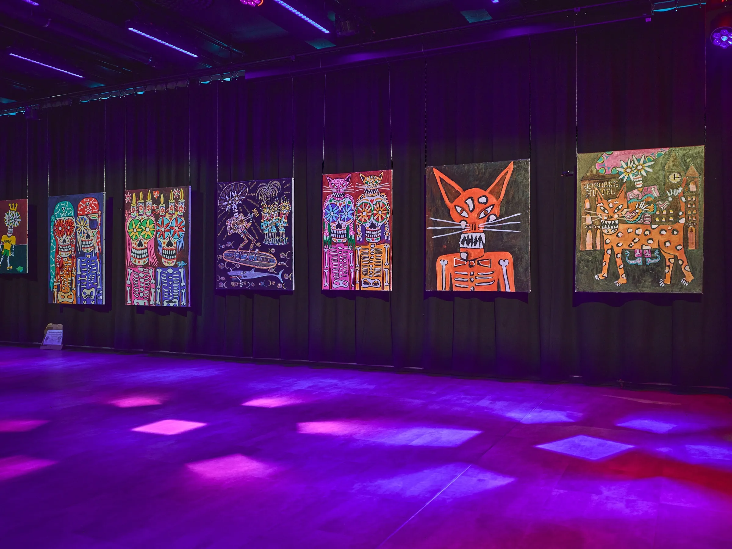 Long wall of colourful paintings in a dark room, patterned light on the floor