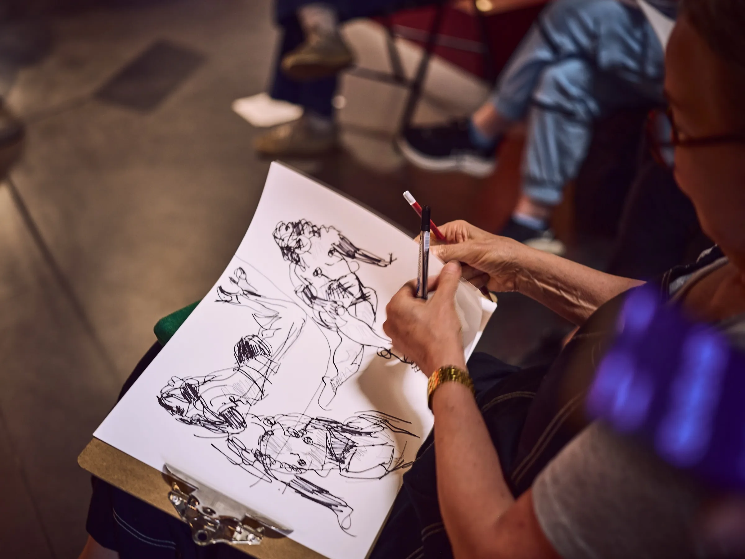 Several quick figure drawings on a sketchpad, with a drawing hand