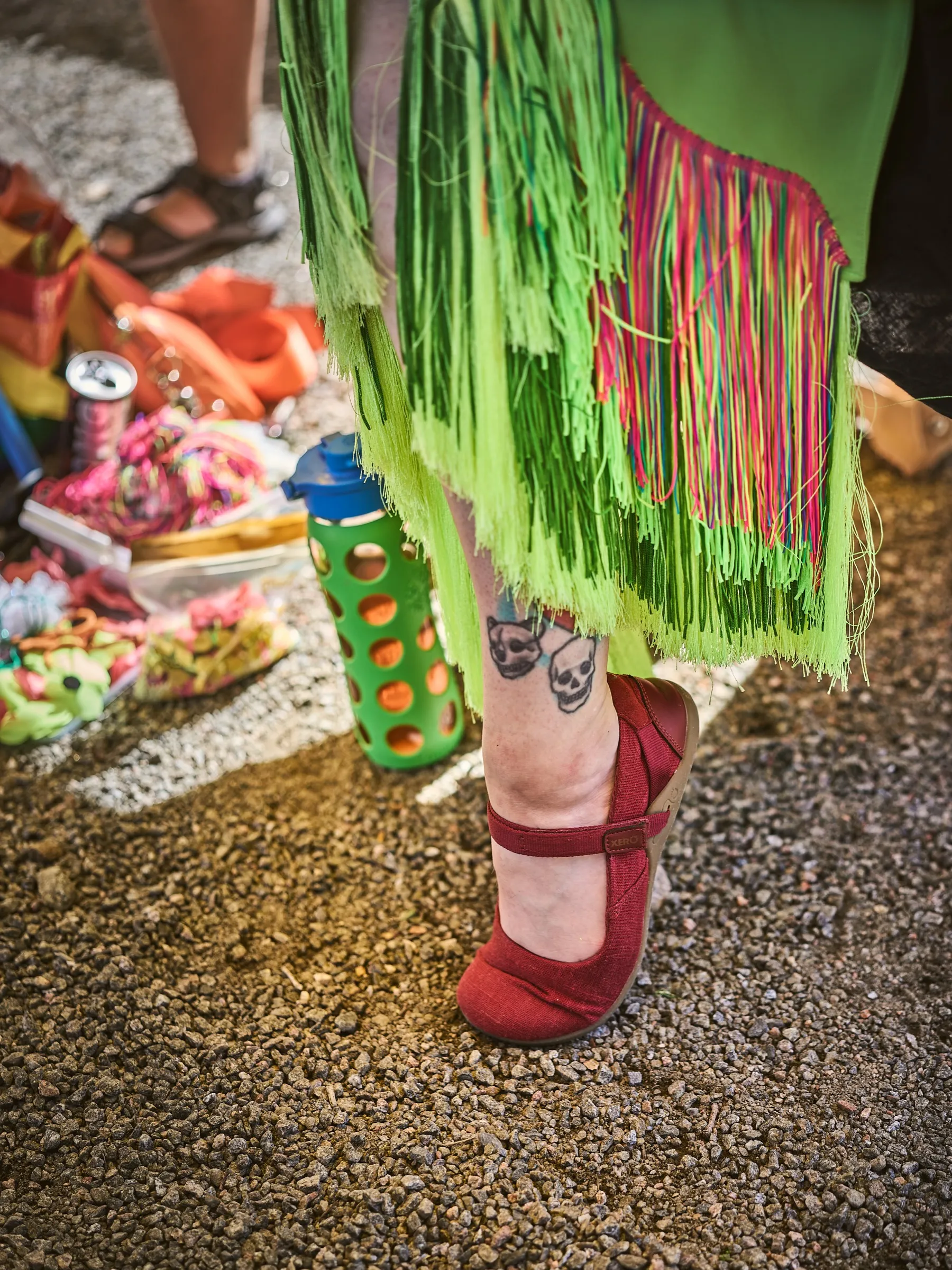 Detail of a colorful fringed costume and red shoes on gravel at the summer festival