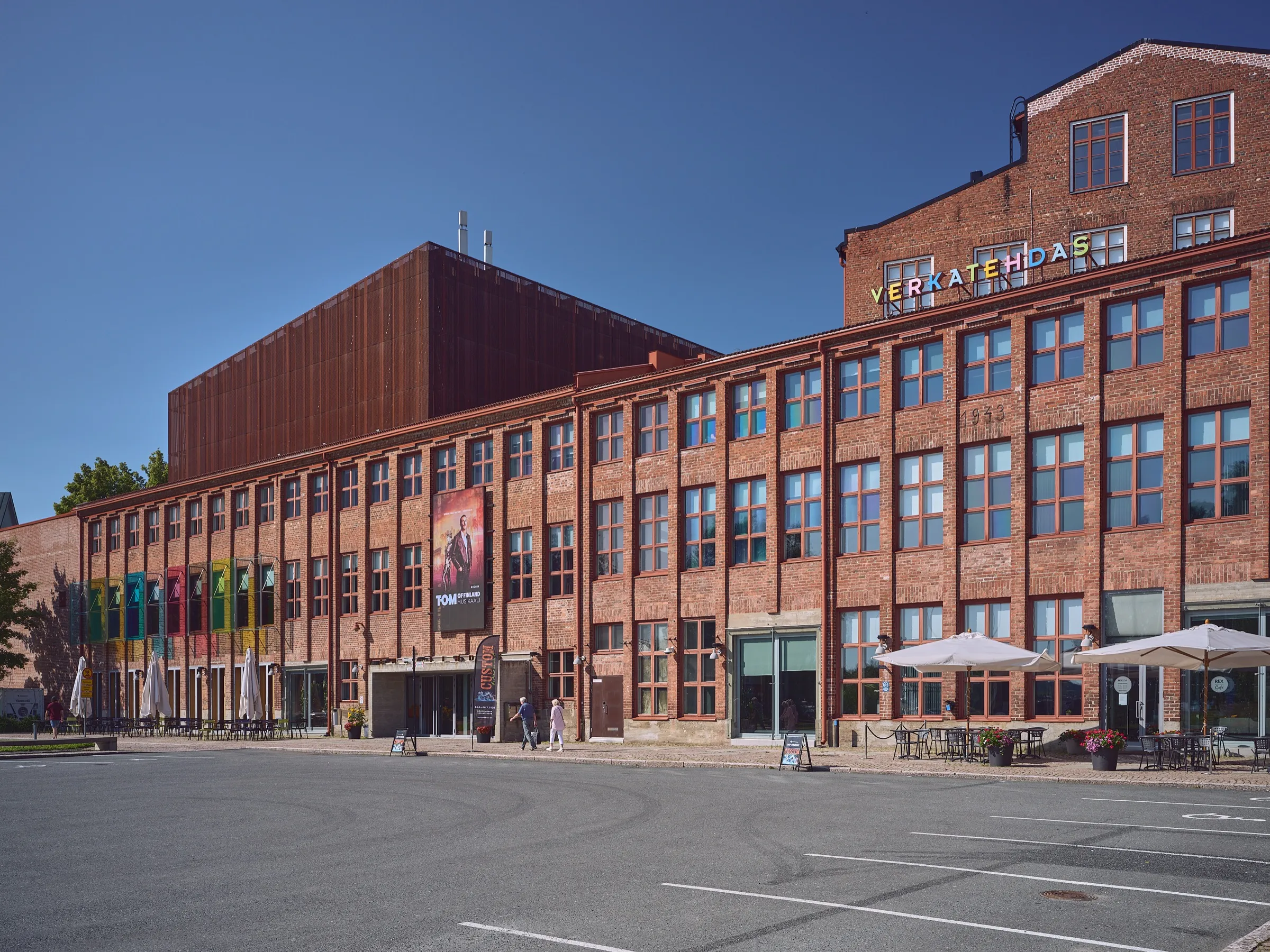 Wide view of the long brick factory Verkatehdas under a blue sky, the colourful VERKATEHDAS lettering above, the year 1933 set into the brickwork on the right