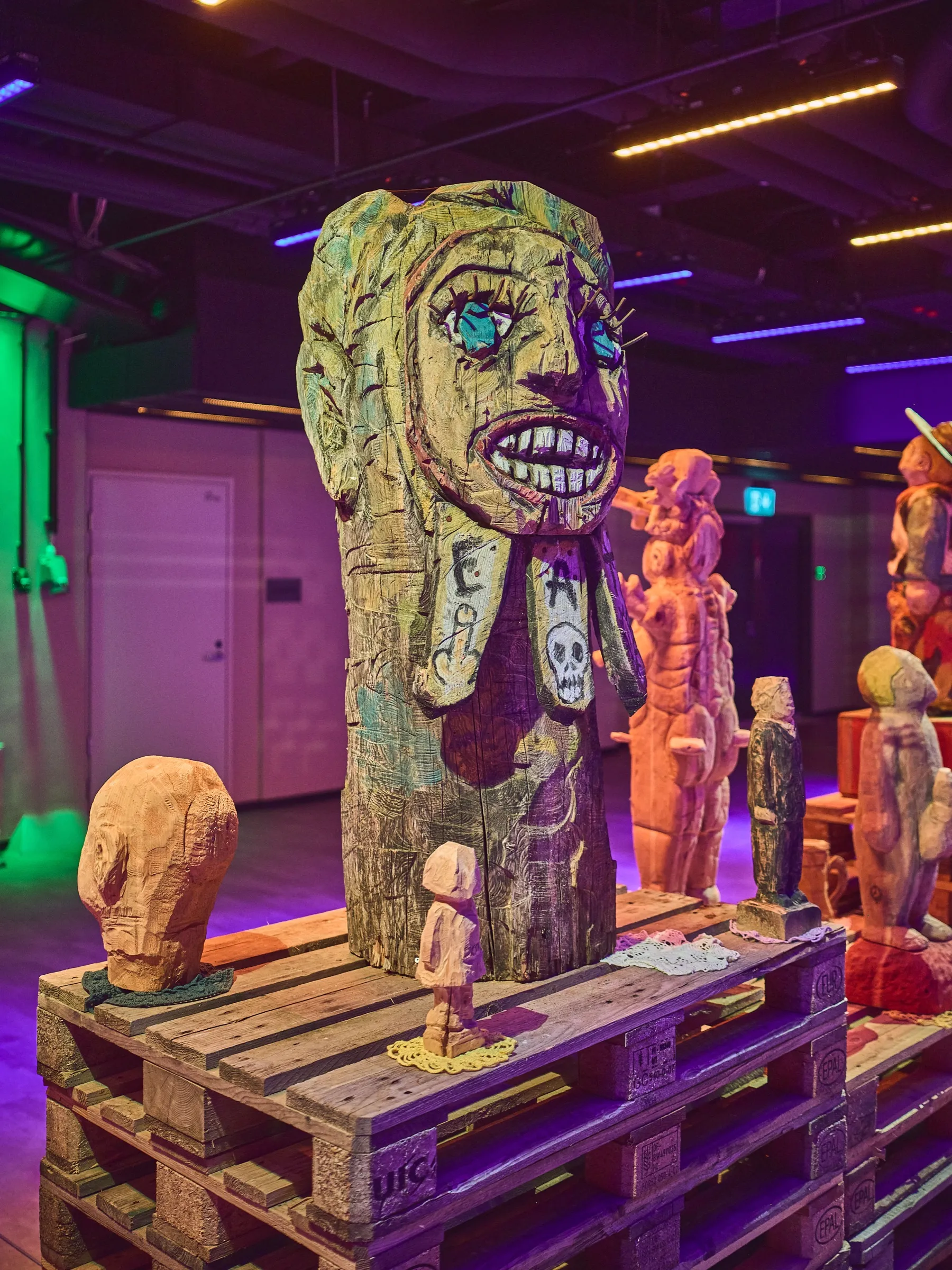 Close wooden figure with a wide toothy grin, lit greenish, more figures behind