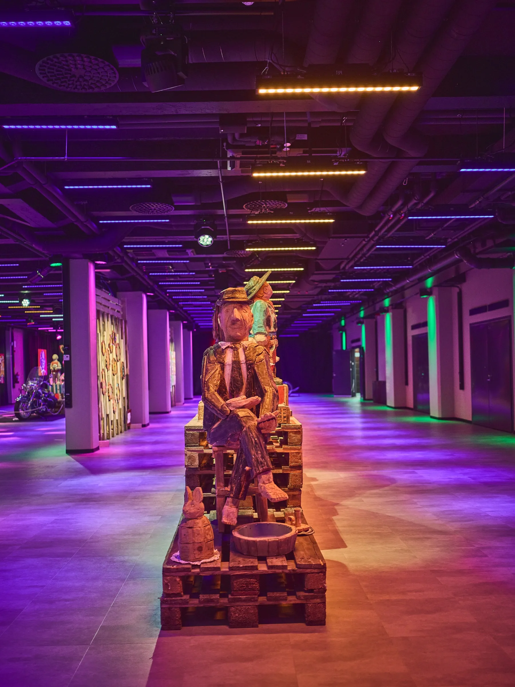 A single seated wooden figure in warm light at the end of a long corridor