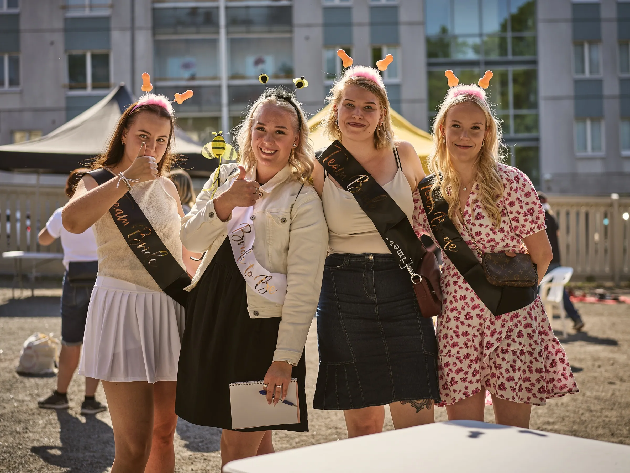 Four young women with Team Bride sashes and joke headbands posing and laughing in the courtyard