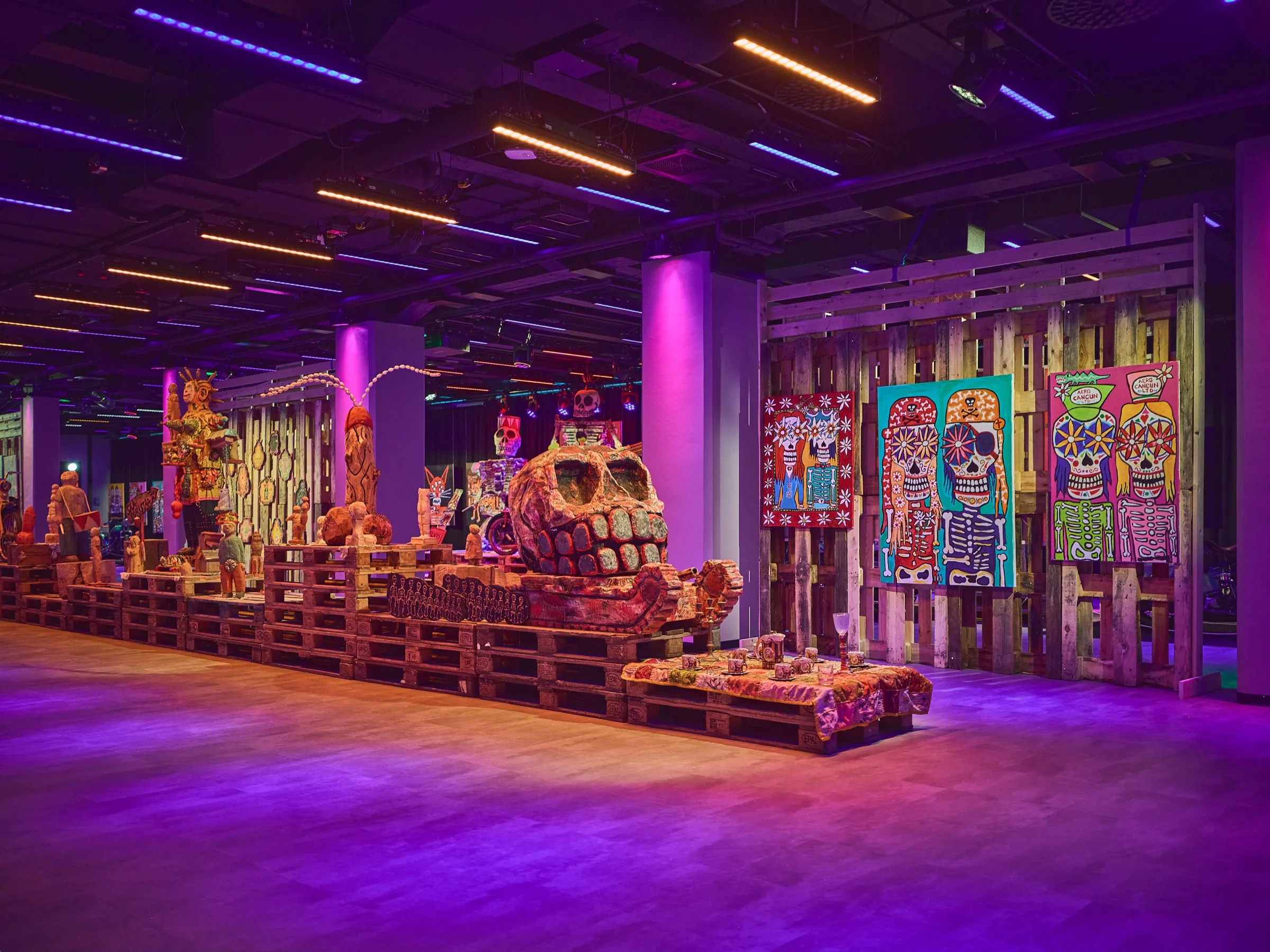 View into the dark Verki exhibition hall with sculptures, paintings and purple light