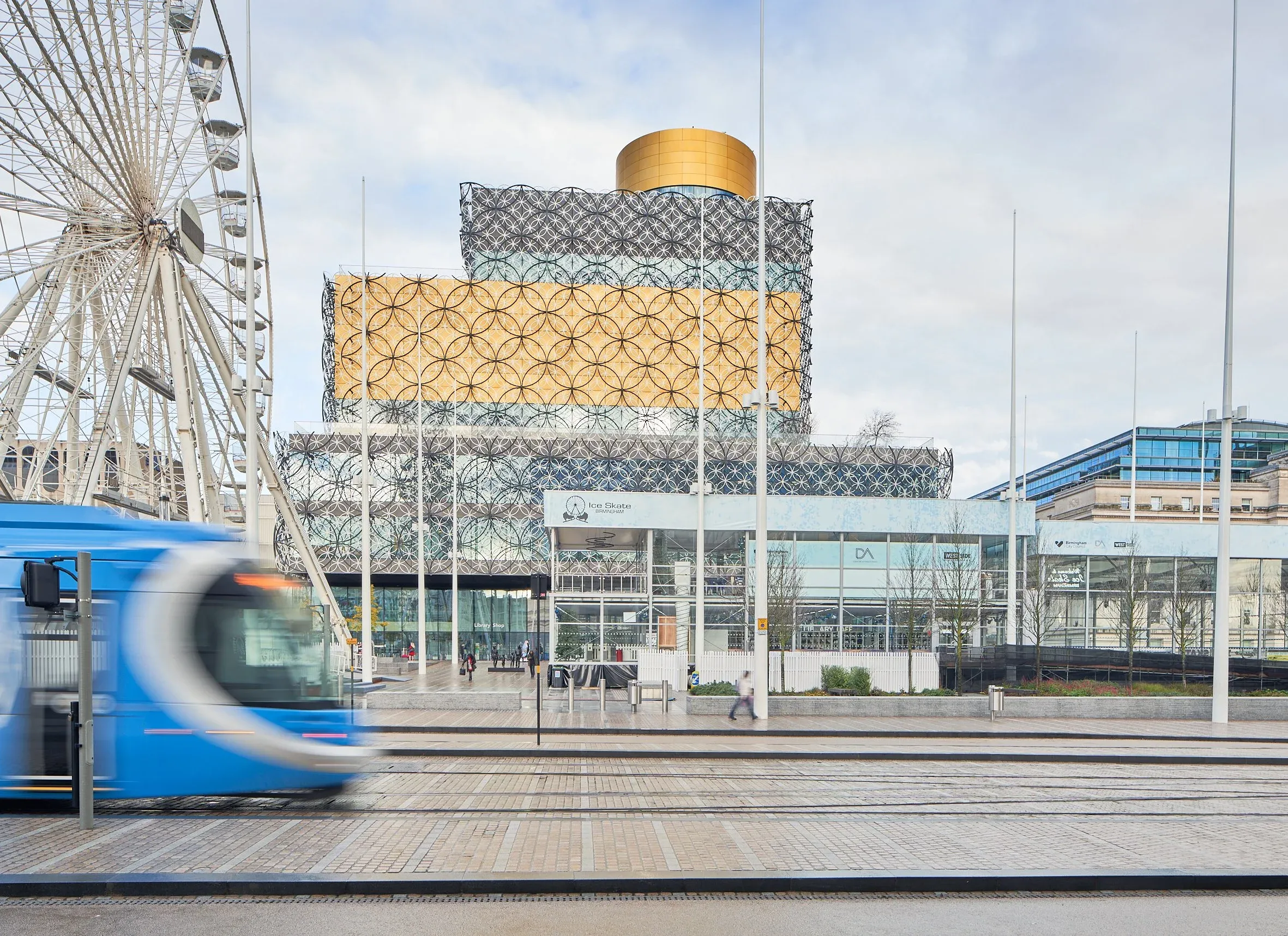 Blaue Straßenbahn fährt vor gemusterter Bibliotheksfassade und Riesenrad, Stadtplatz, Bodenaufnahme