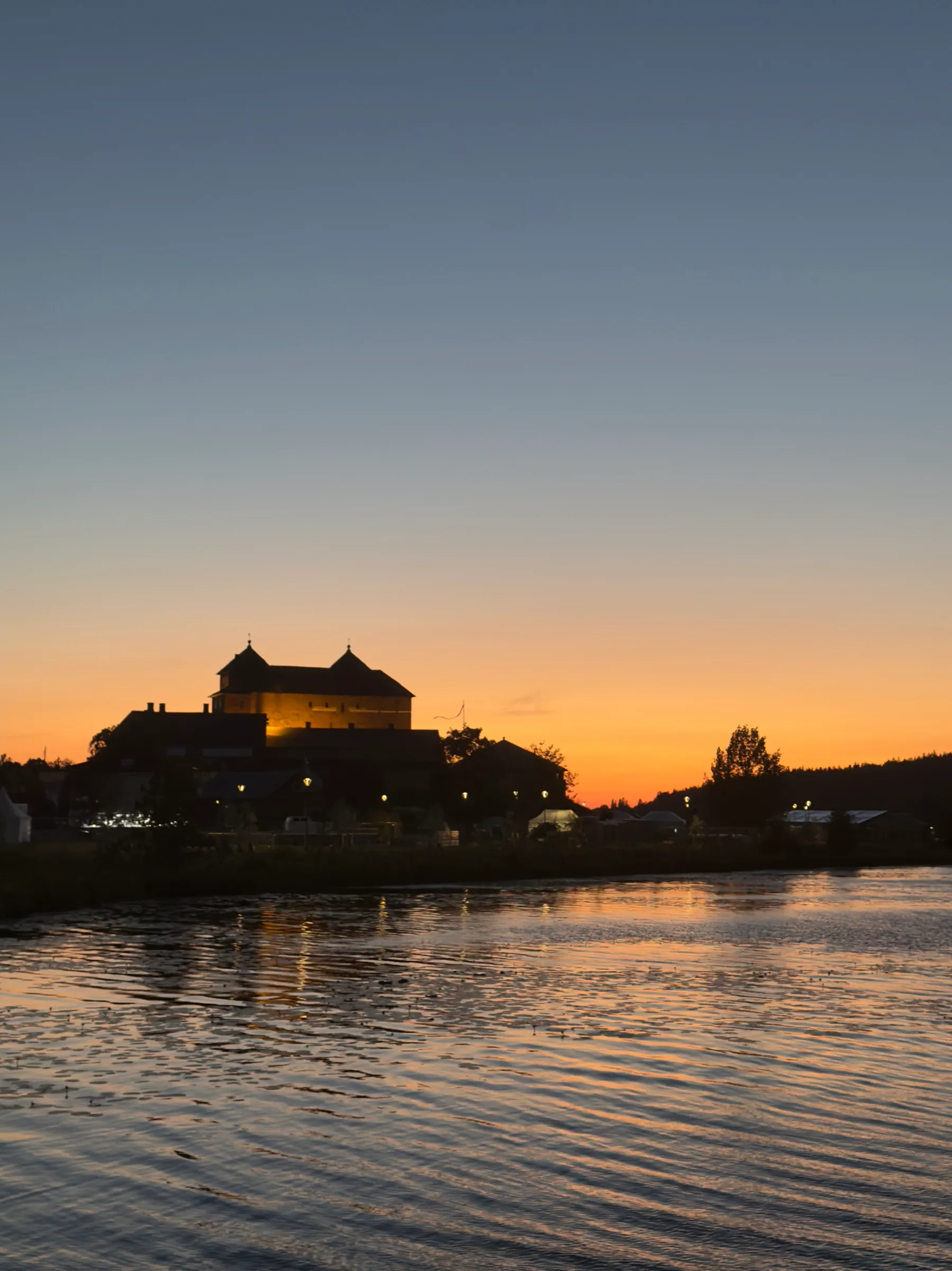 Häme Castle as a dark silhouette above the lake, an orange glowing night sky behind it, portrait format