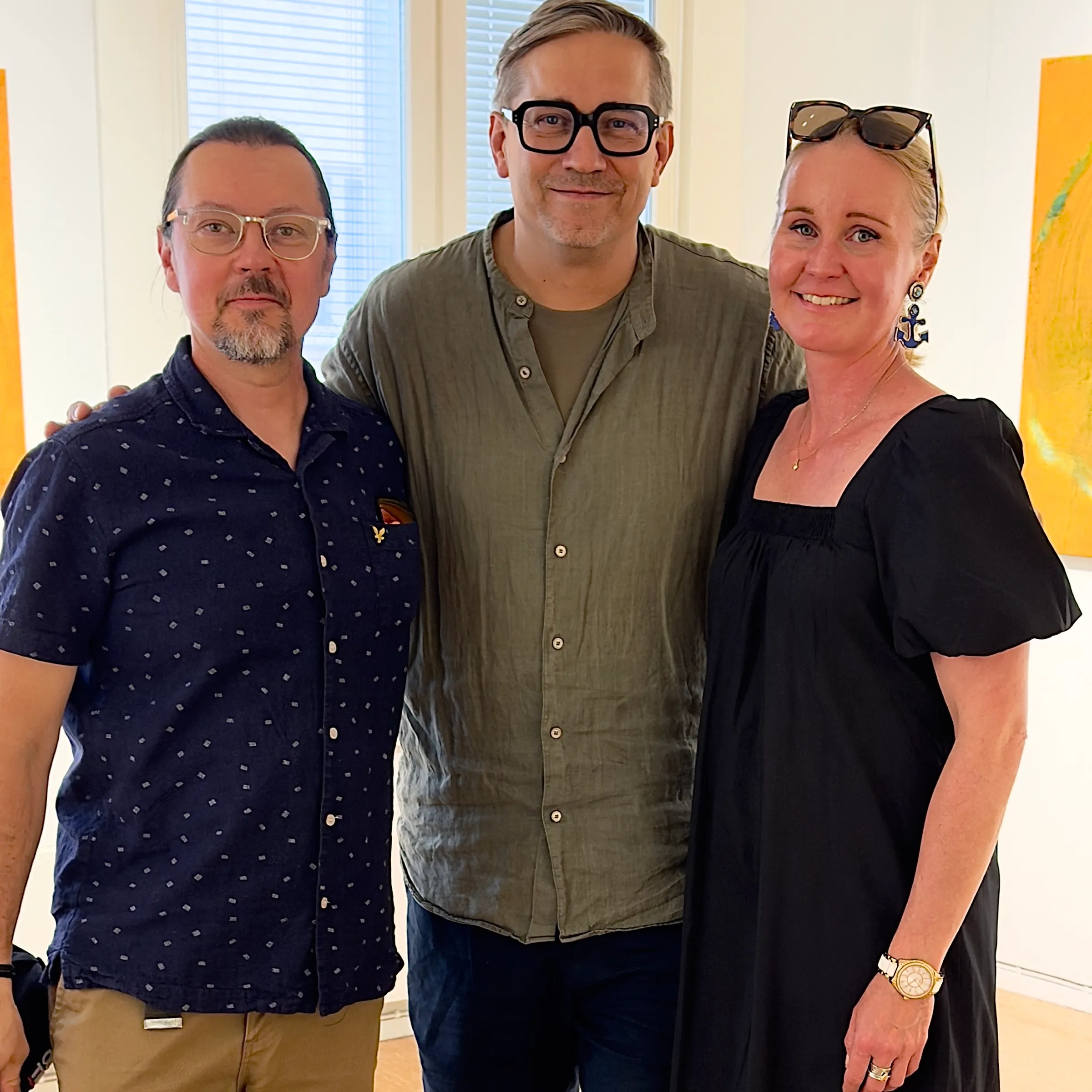 Sami, Roman and Kathri standing side by side, smiling, in a bright gallery room, portrait format