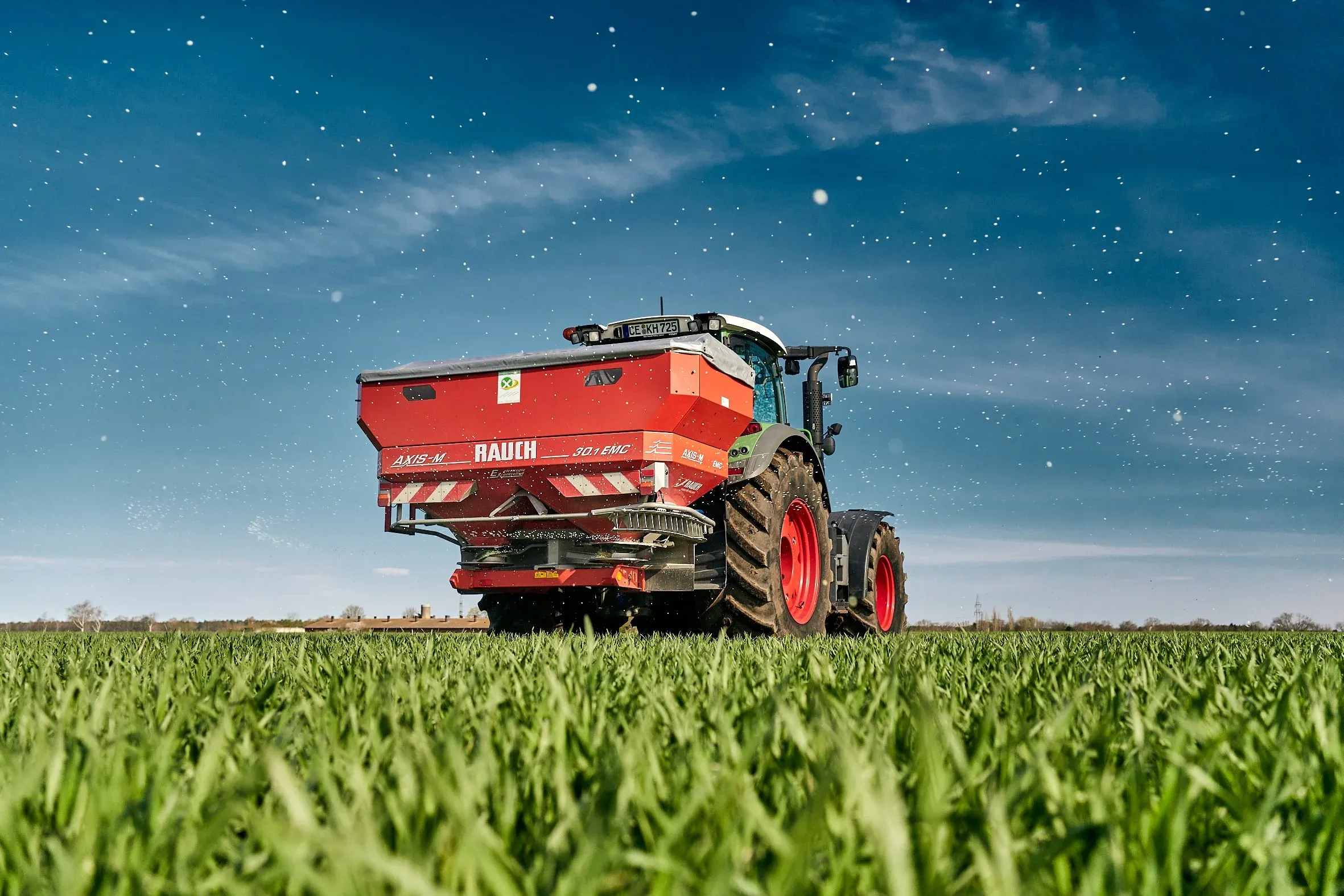 Roter Düngerstreuer an einem Traktor auf grünem Feld unter dunkelblauem Himmel, Bodenaufnahme im Abendlicht