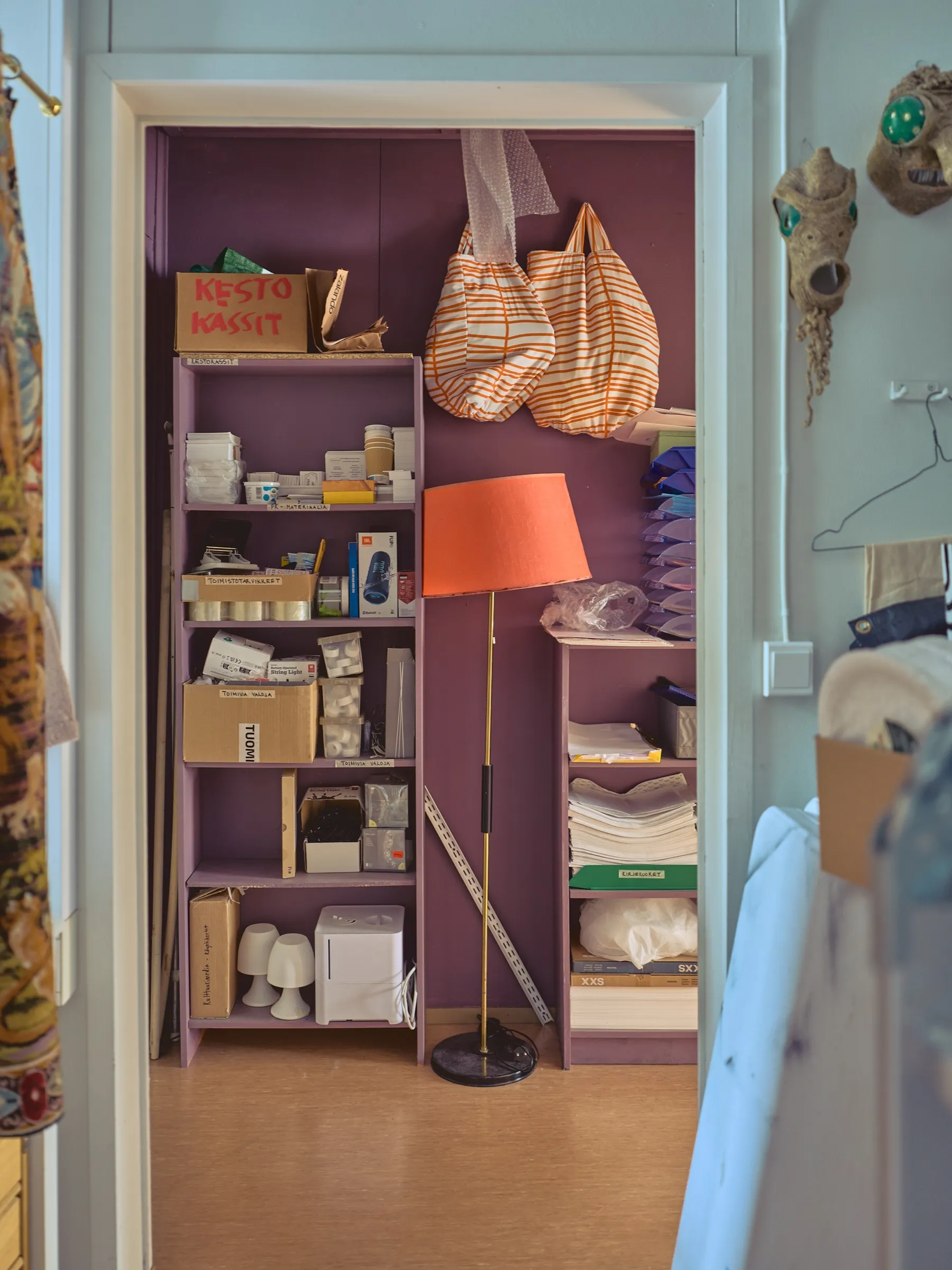 View into the storage room with purple shelves, fabric bags and a floor lamp with an orange shade