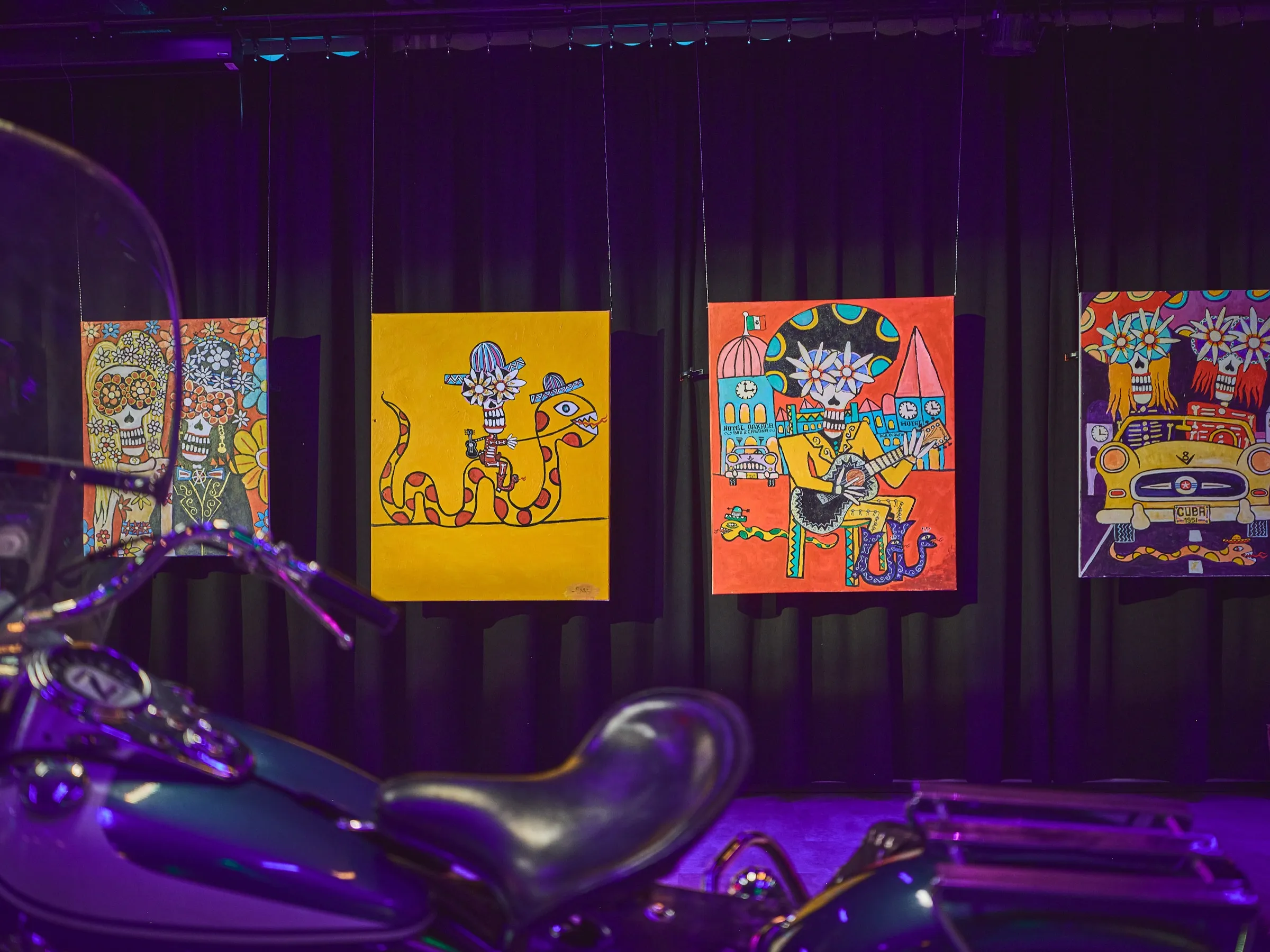 Dark chopper in the foreground, small colourful paintings on the wall behind