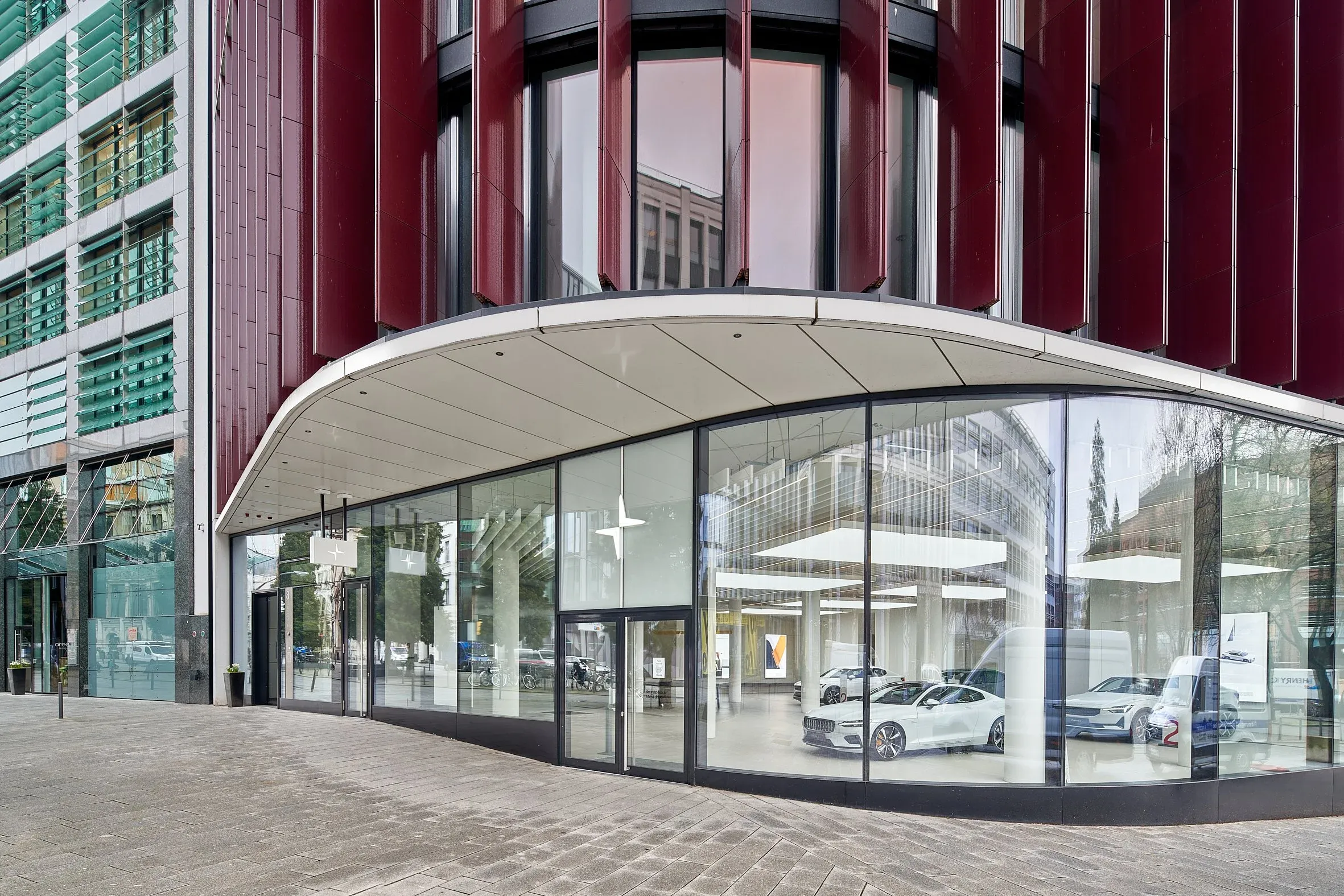 Außenansicht des Polestar Space in Hamburg, gerundete Glasfassade unter rotem Gebäudebogen, Showroom hinter der Scheibe