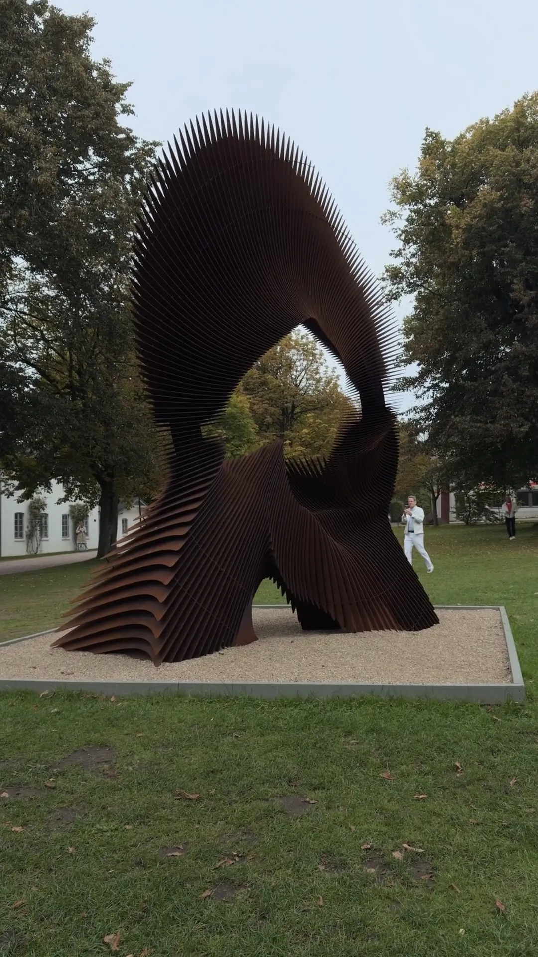 The camera approaches Jan Dostál's sculpture of curved Corten steel slats in the park