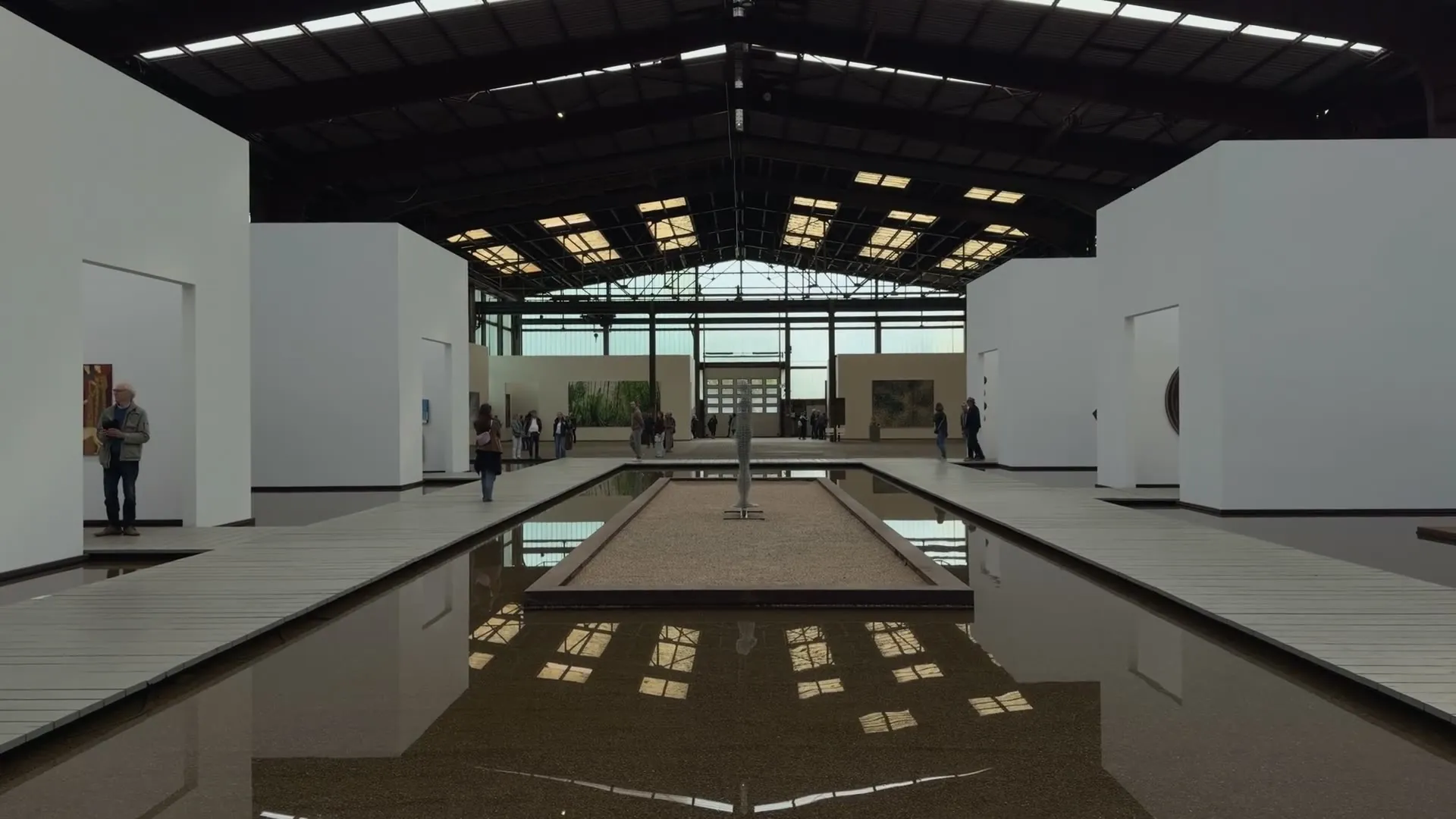 A camera move along the wooden walkway between white exhibition cubes and water basins