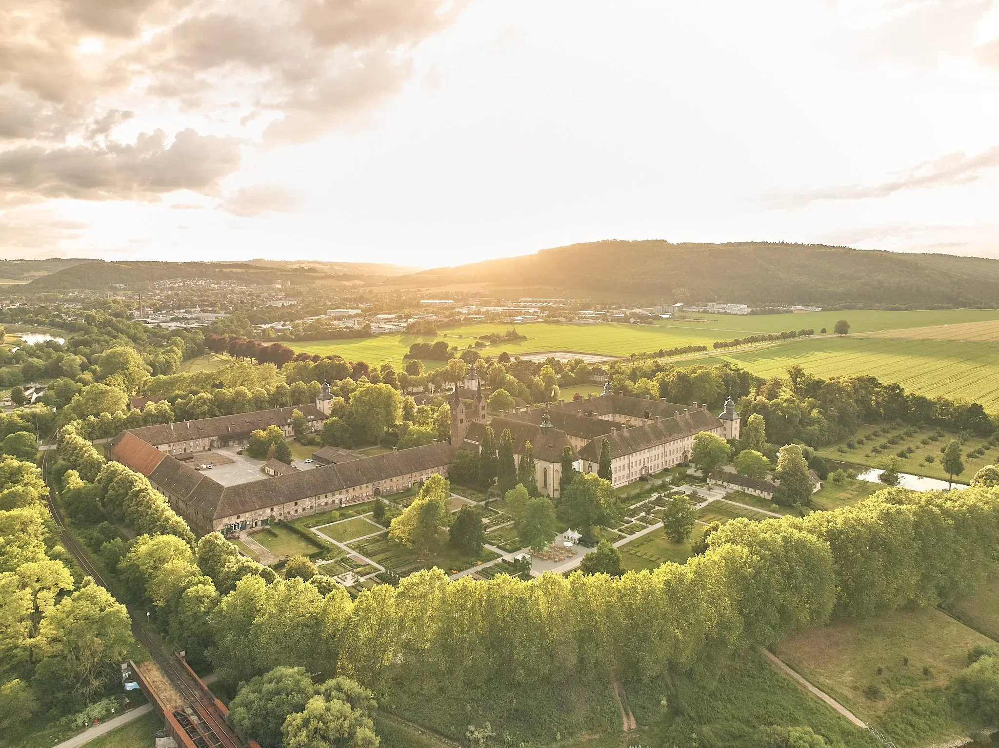 Luftaufnahme der Klosteranlage Corvey in Höxter mit Remtergarten, umgebenden Wiesen und Feldern im Gegenlicht der Abendsonne