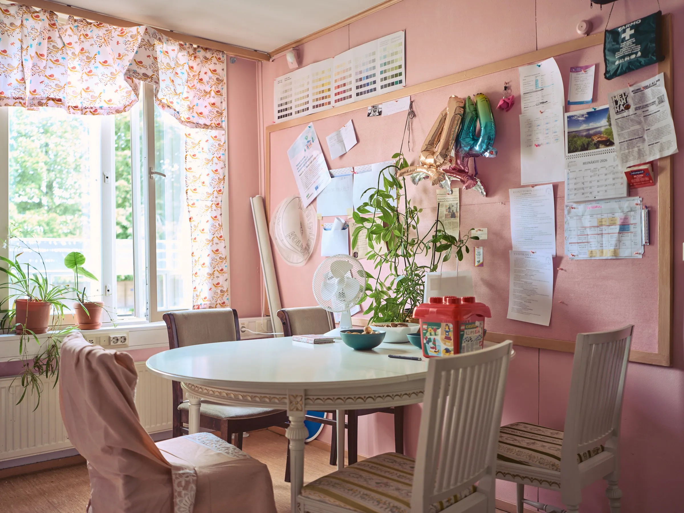 Pink meeting room with a round white table, a large pinboard and plants by the window