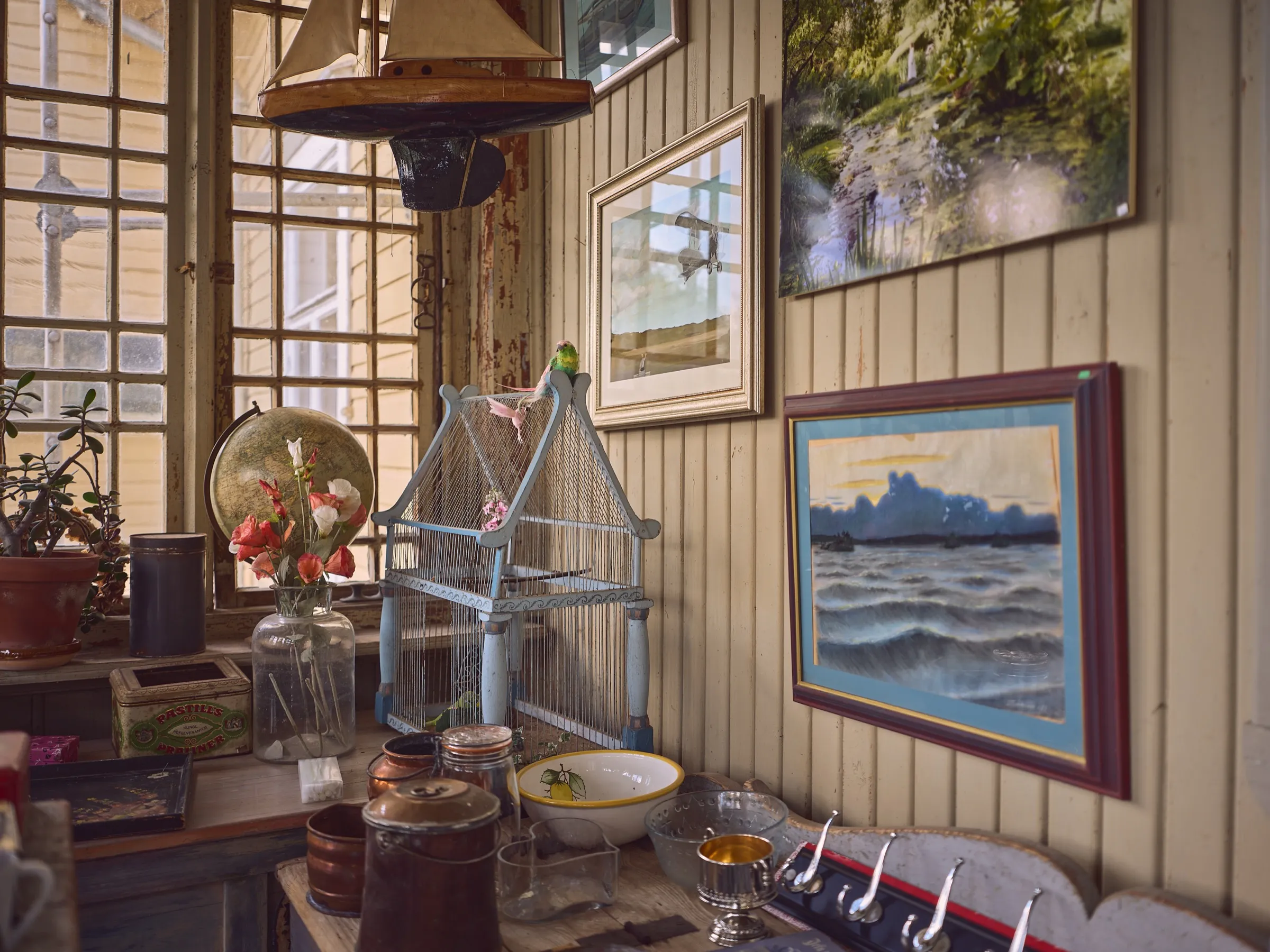 Veranda wall with framed landscape paintings, a wire birdcage in front