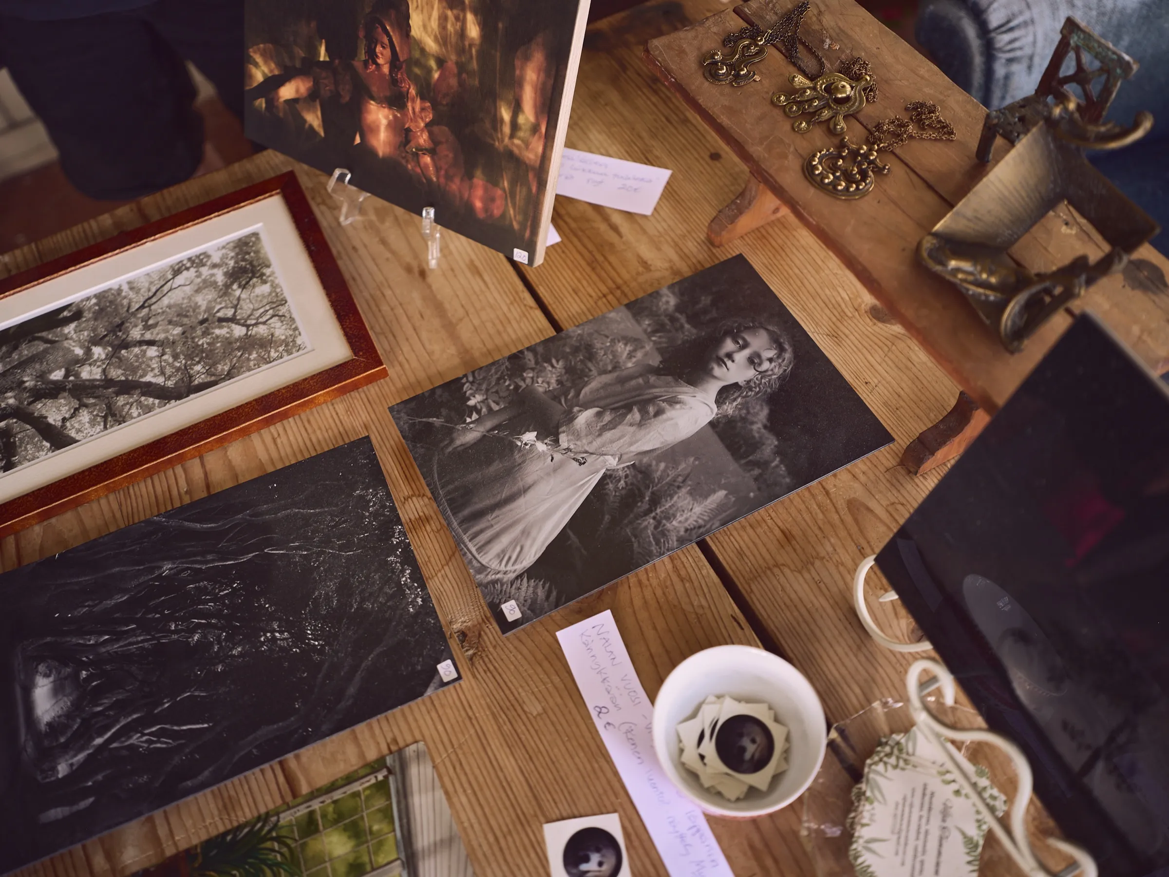 Table top full of framed pictures and prints, a coffee cup among them