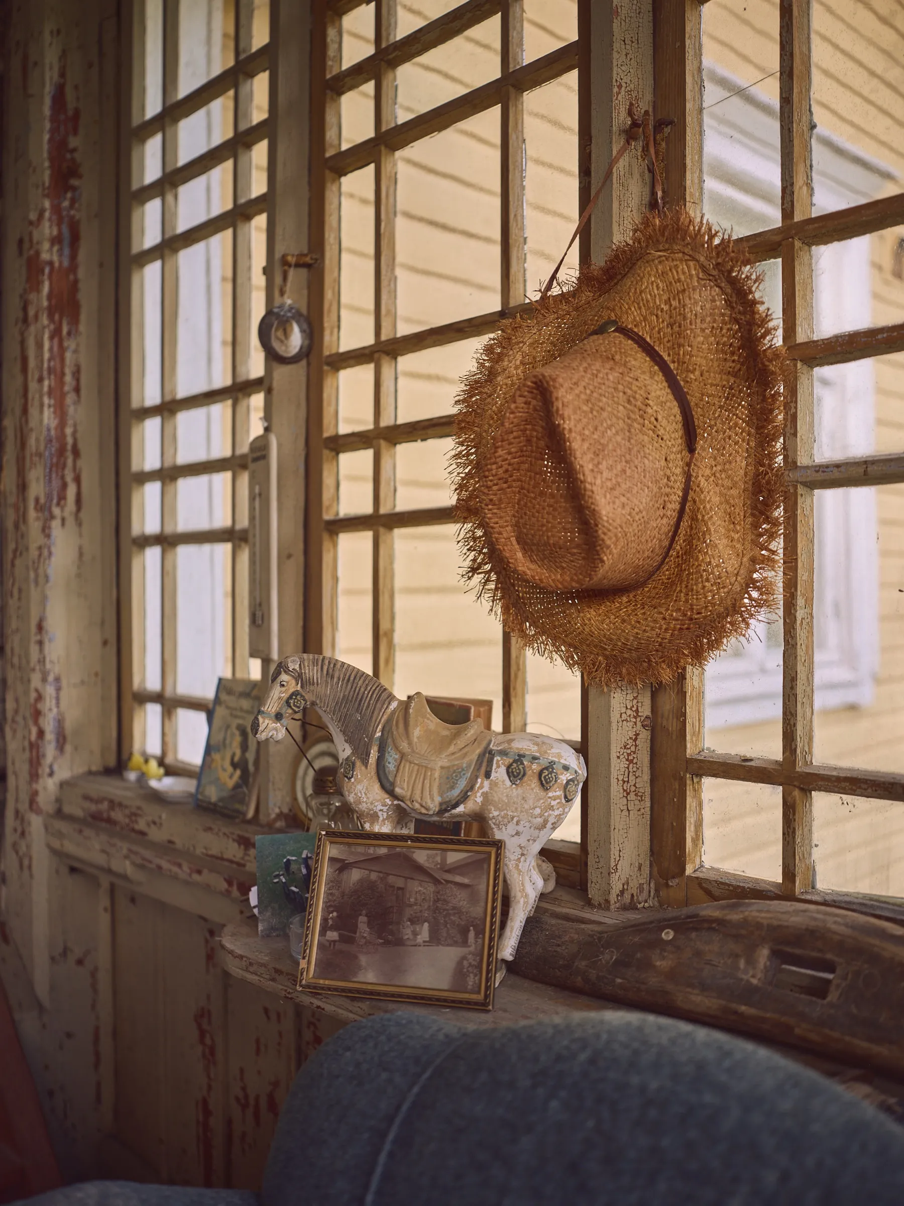 Straw hat hanging on the veranda's lattice window, old finds in front, portrait format