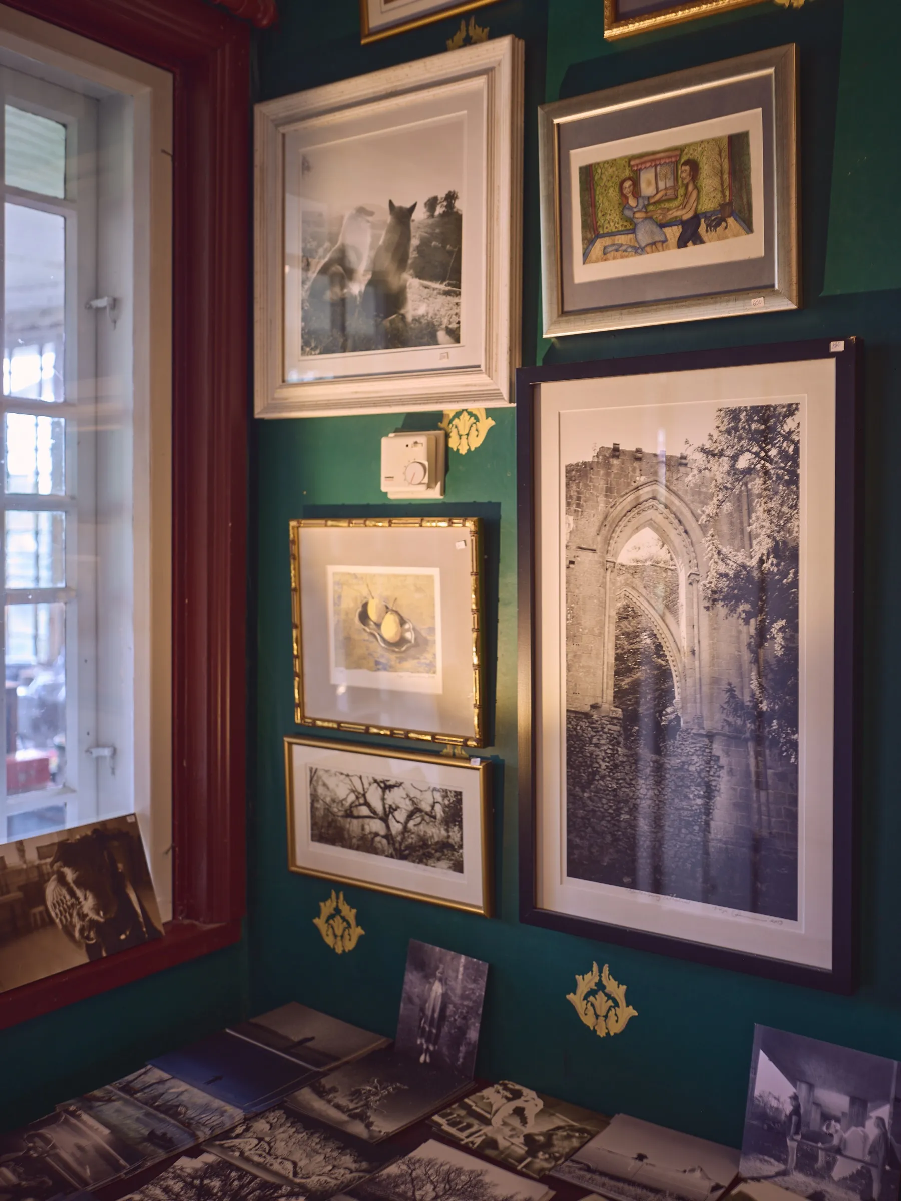 Green wall densely hung with framed photographs and prints, portrait format