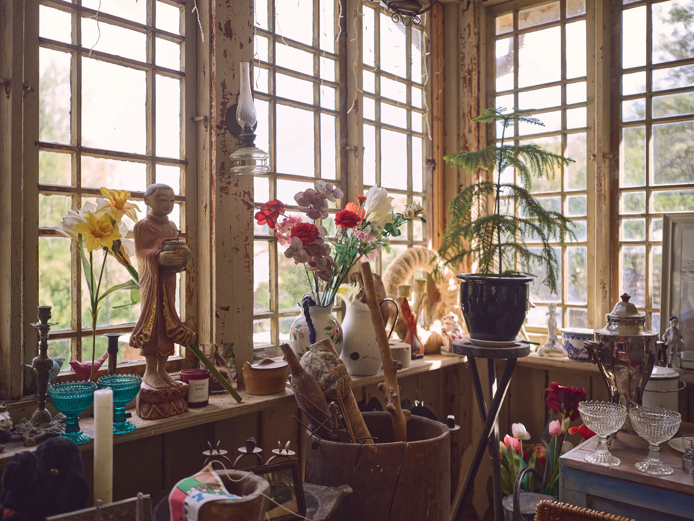 Veranda windowsill with artificial flowers, figures and vases against the light