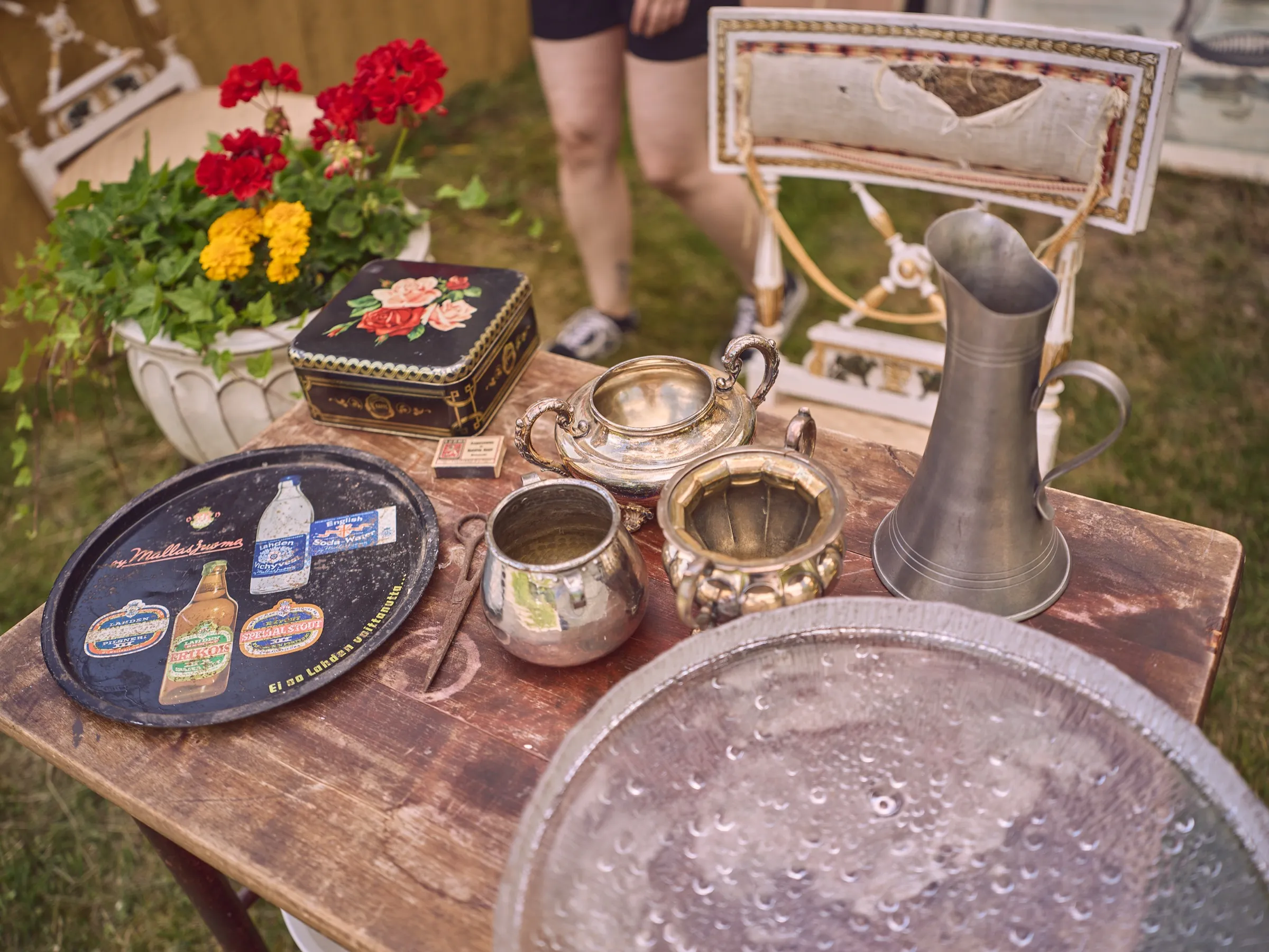 Flea market table with silver jugs, trays, flowers and a large glass plate