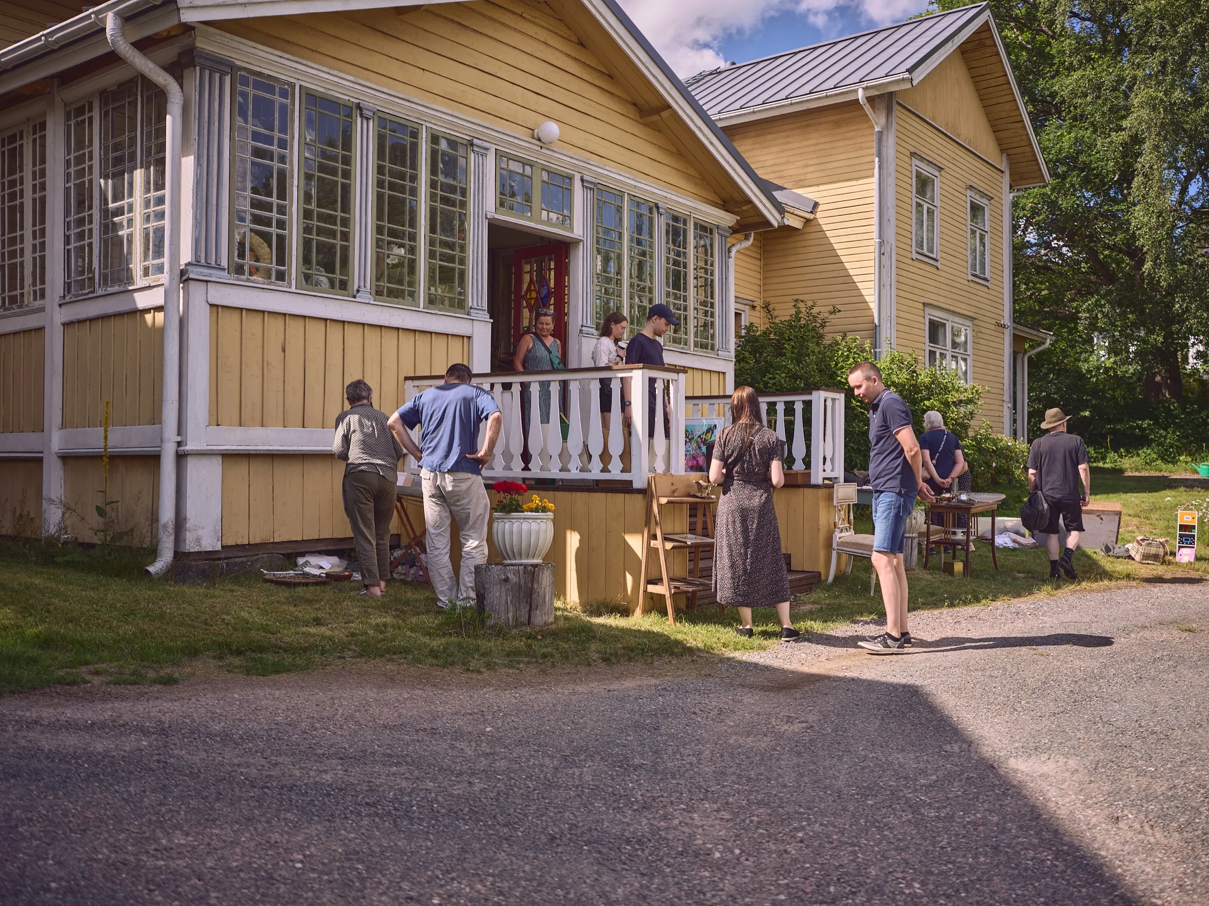 Visitors browsing between the stalls in front of the yellow house's veranda