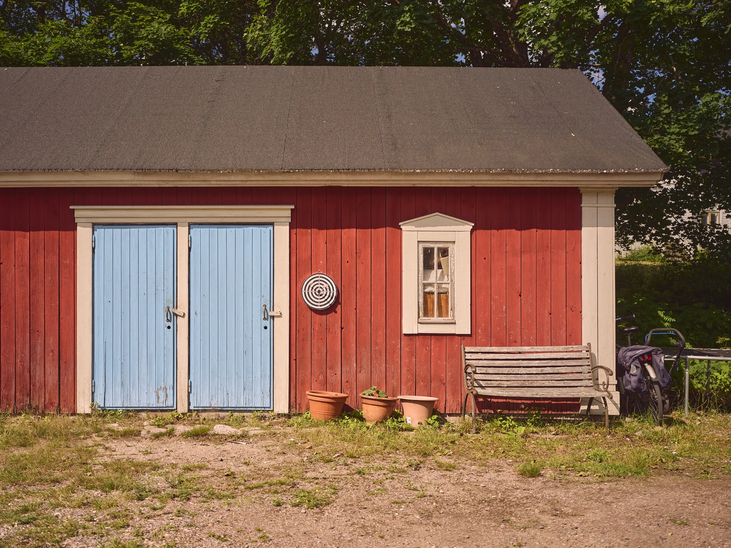 Red wooden barn with light blue doors, flower pots and a bench in front